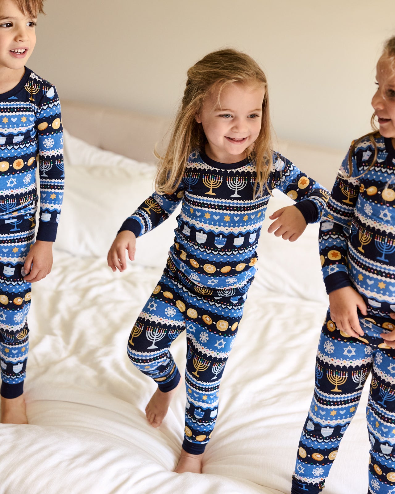 Group of three kids wearing Hanukkah Fair Isle Two-Piece Pajama Sets on a white bed