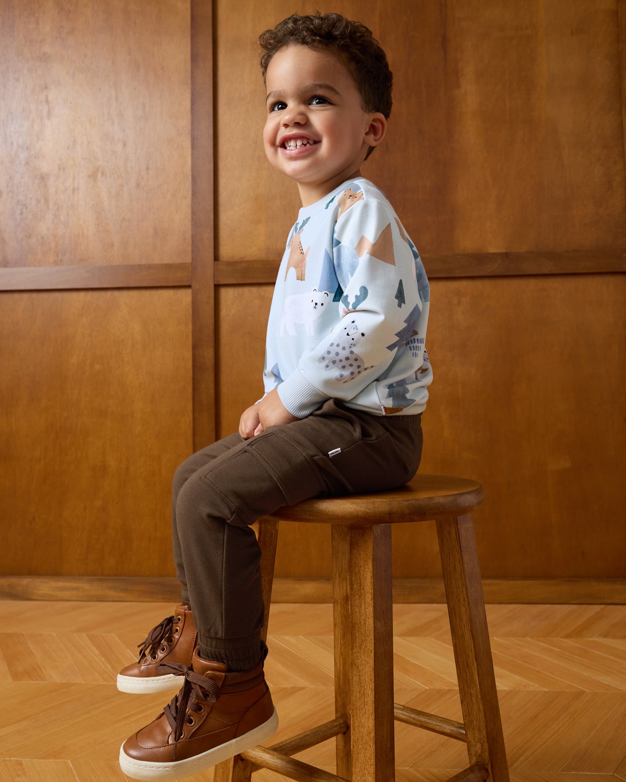 Boy sitting on a wooden stool wearing the Alpine Explorers Crewneck Sweatshirt