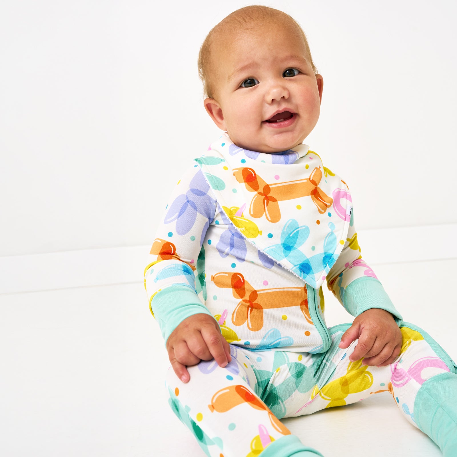 Sitting child wearing the Balloon Bash Bandana Bib and matching zipper pajamas