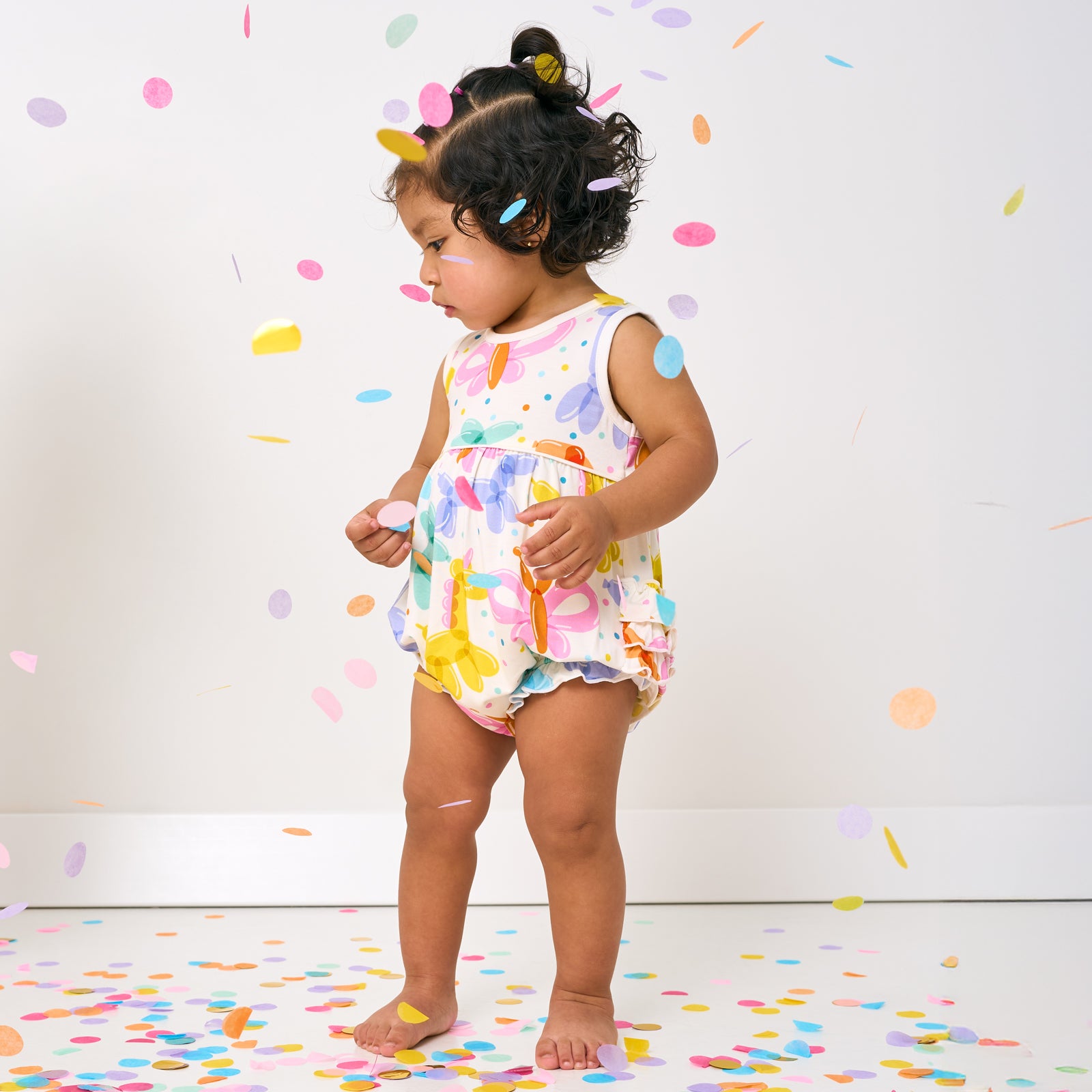 Standing child wearing the Balloon Bash Bubble Romper with confetti falling