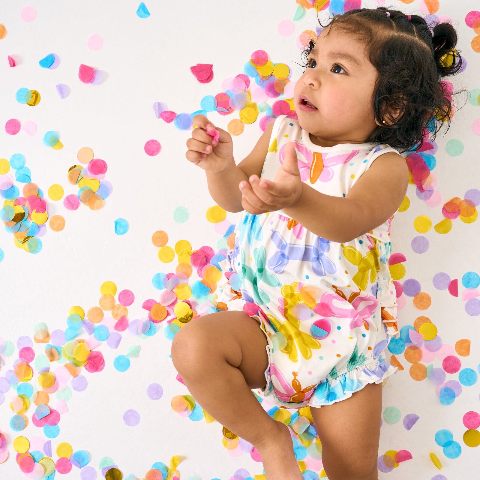 Aerial view of child wearing the Balloon Bash Bubble Romper with confetti around her