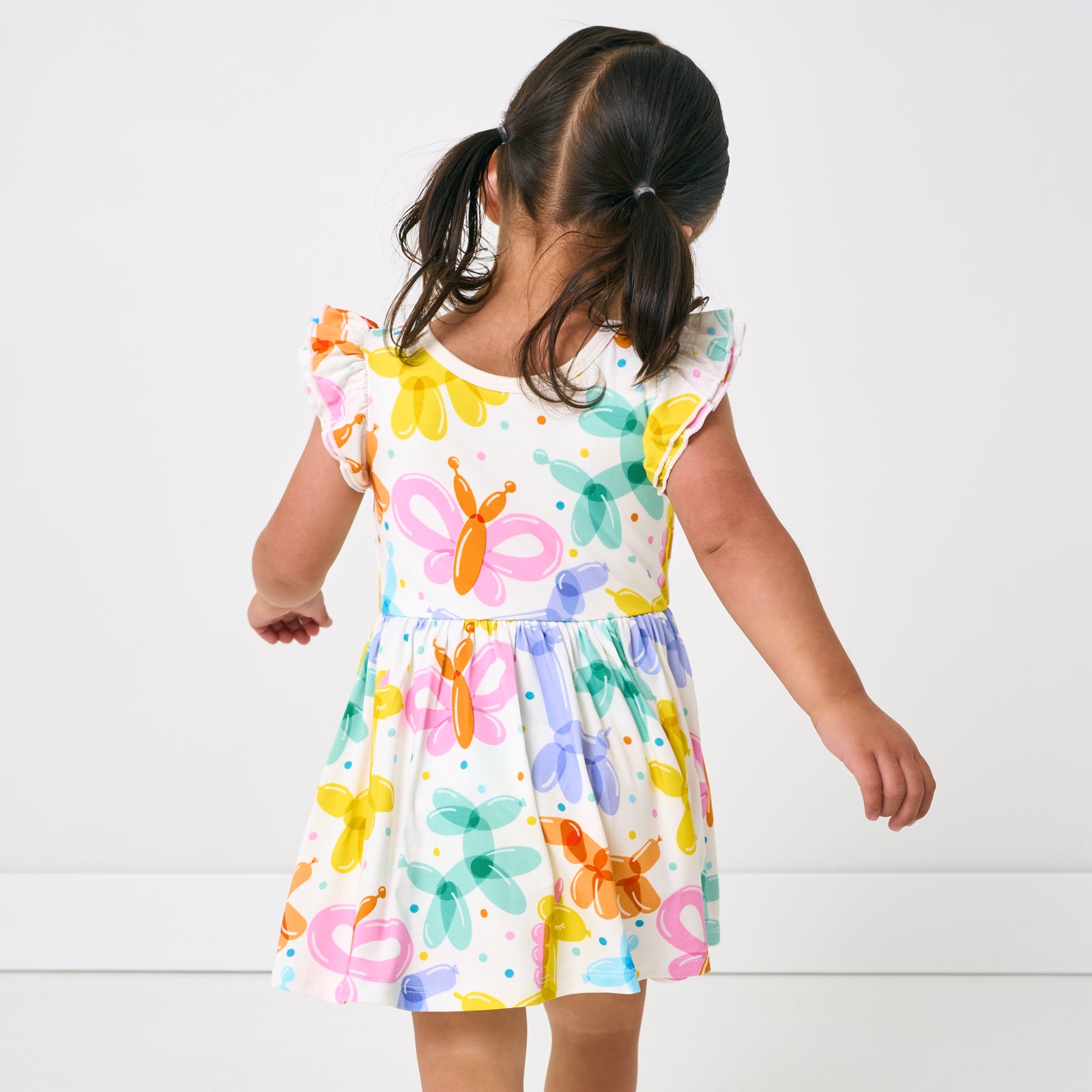 Back view of child wearing the Balloon Bash Flutter Twirl Dress with Bodysuit