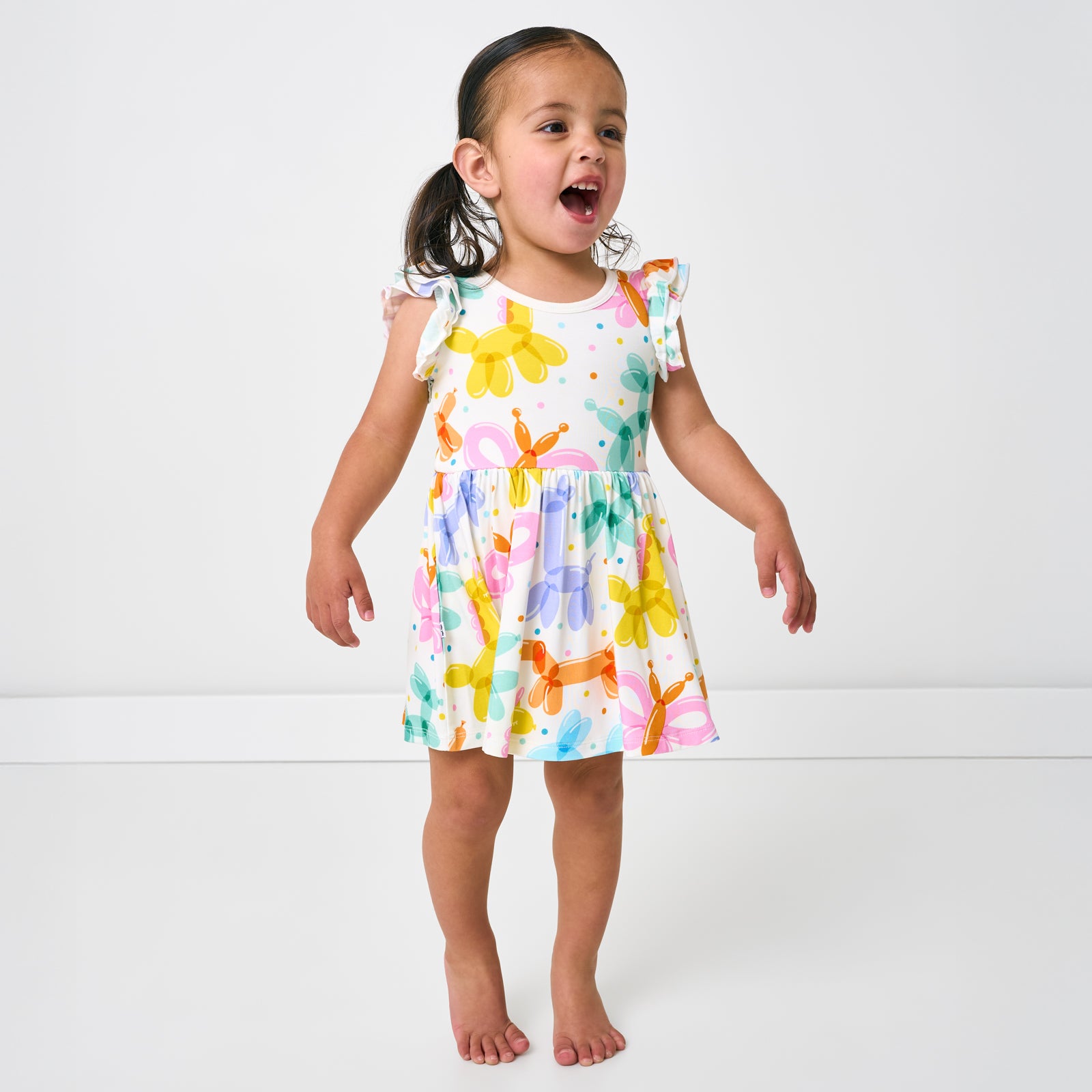 Standing child wearing the Balloon Bash Flutter Twirl Dress with Bodysuit