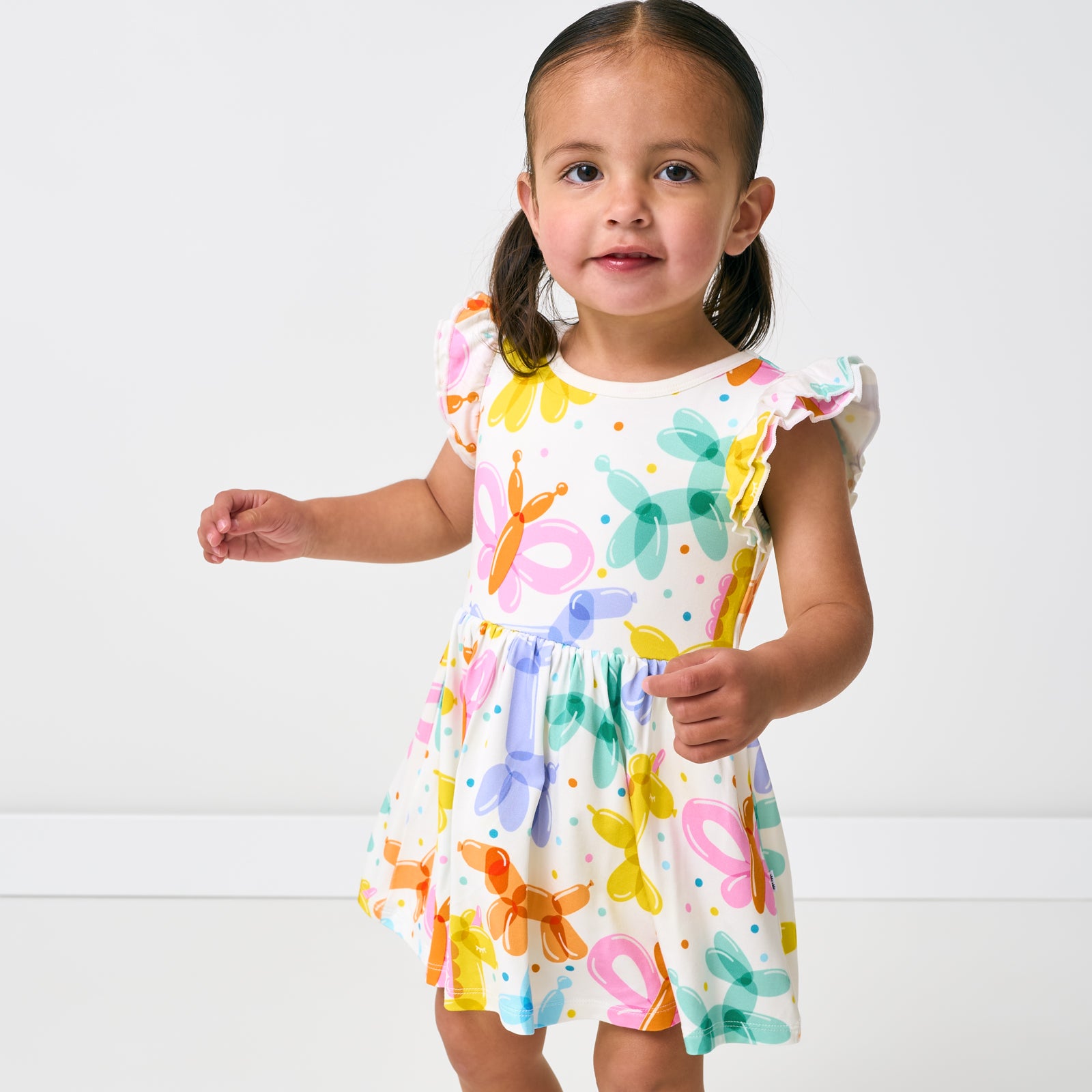 Close up of standing child wearing the Balloon Bash Flutter Twirl Dress with Bodysuit