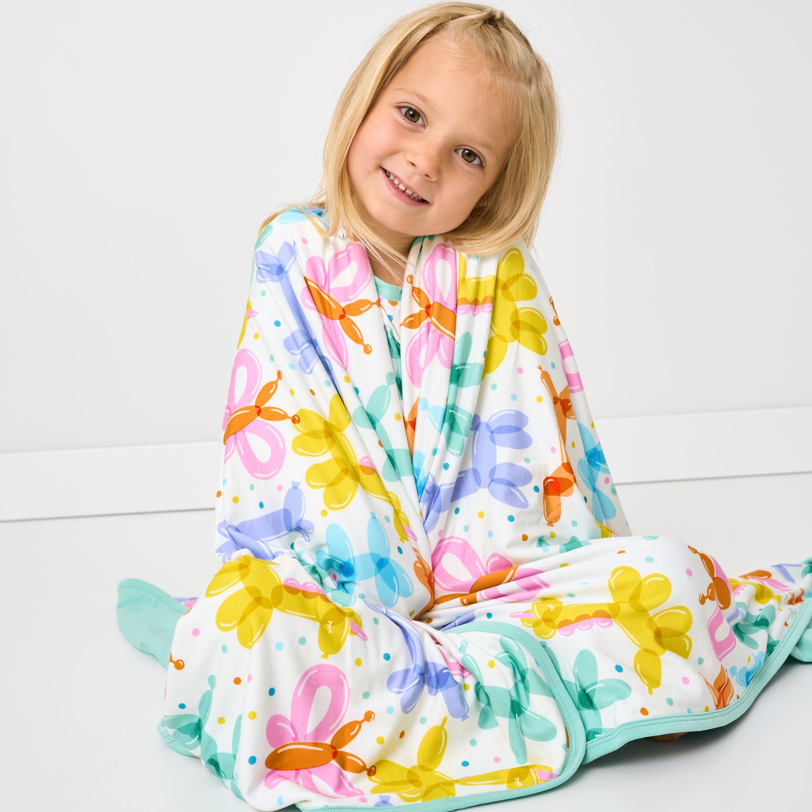 Sitting child wrapped in the Balloon Bash Large Cloud Blanket®