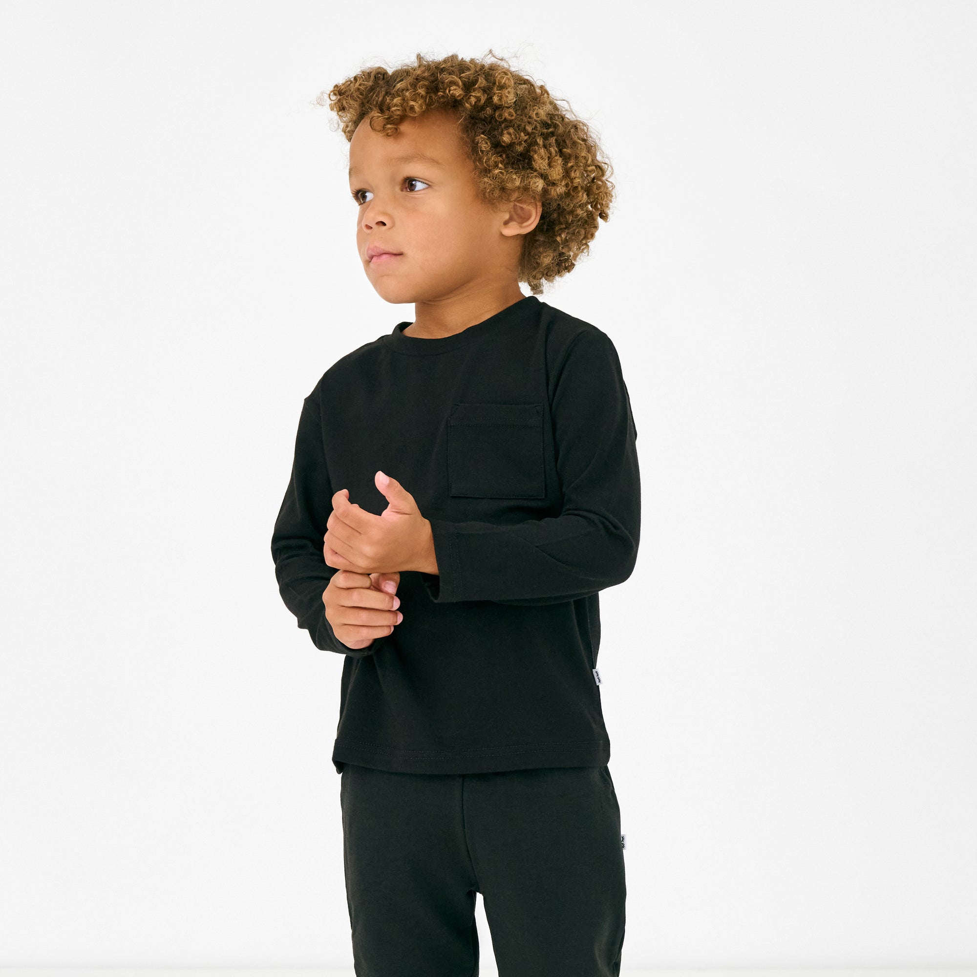 Standing child wearing the Black Long Sleeve Relaxed Pocket Tee