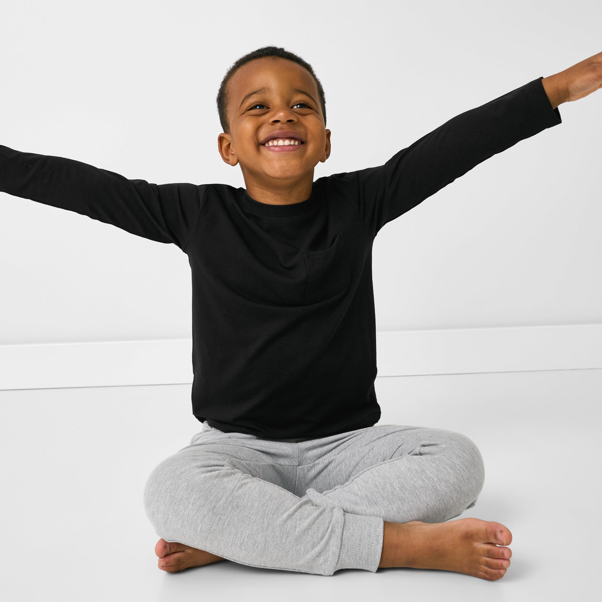 Sitting child wearing the Black Long Sleeve Relaxed Pocket Tee with gray joggers