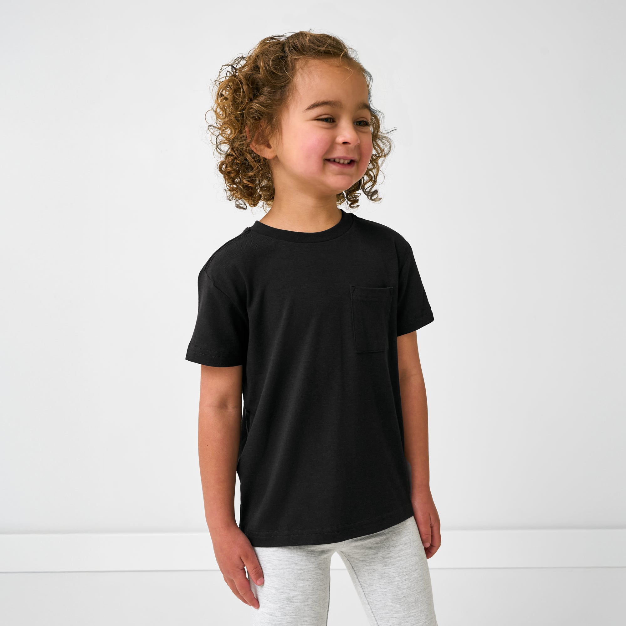 Standing girl wearing the Black Short Sleeve Relaxed Pocket Tee with gray leggings