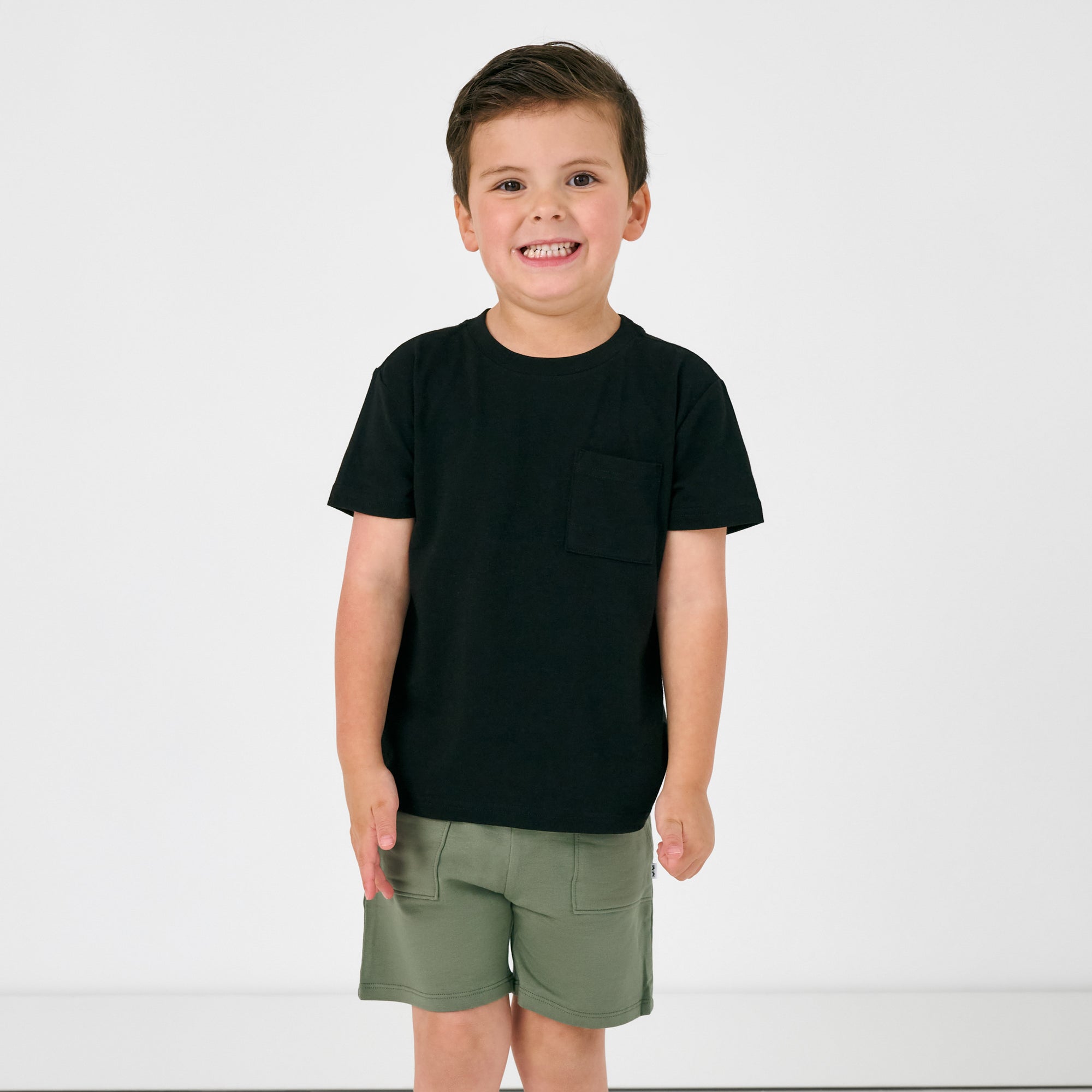 Standing boy wearing the Black Short Sleeve Relaxed Pocket Tee with green shorts
