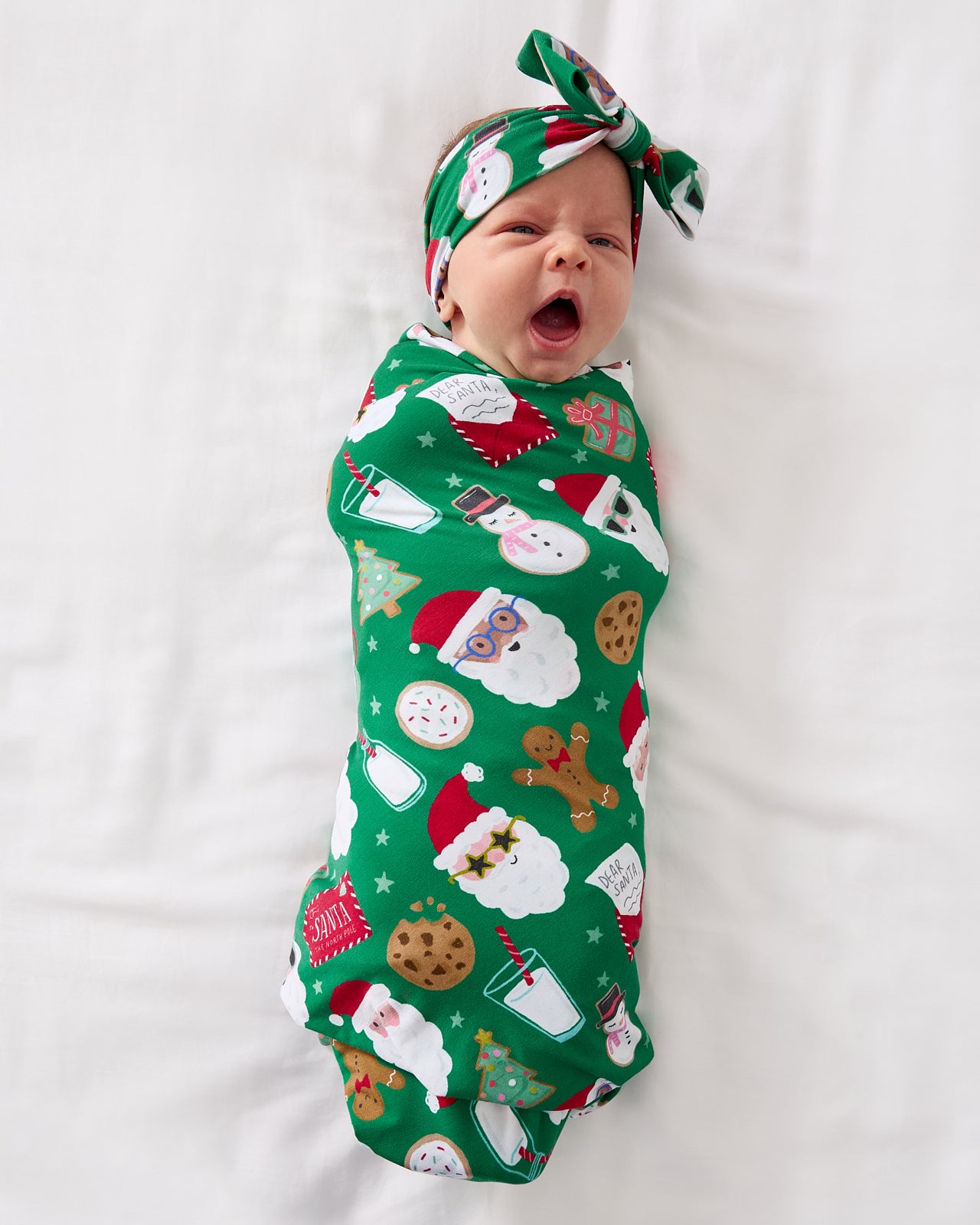 Yawning baby wearing the Cookies for Santa Swaddle & Luxe Bow Headband Set