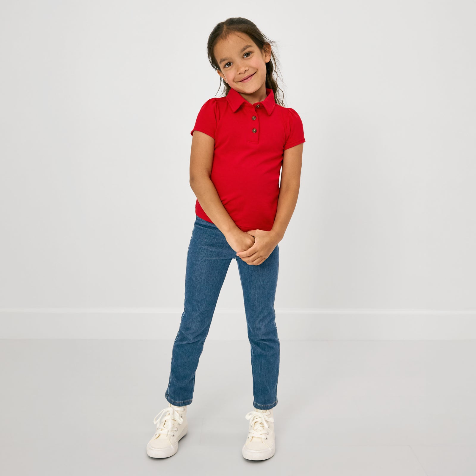 Standing child wearing the Candy Red Puff Sleeve Polo and blue denim jeggings