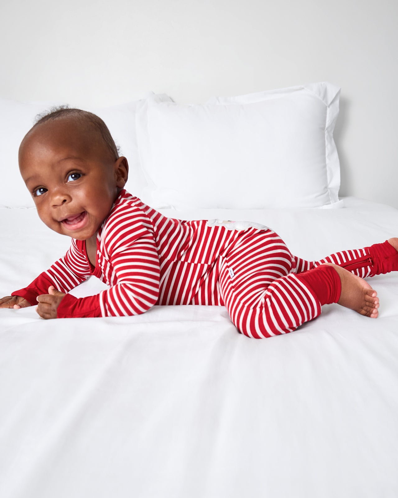 Alternate baby wearing the Candy Cane Stripe Crescent Zippy on a white bed