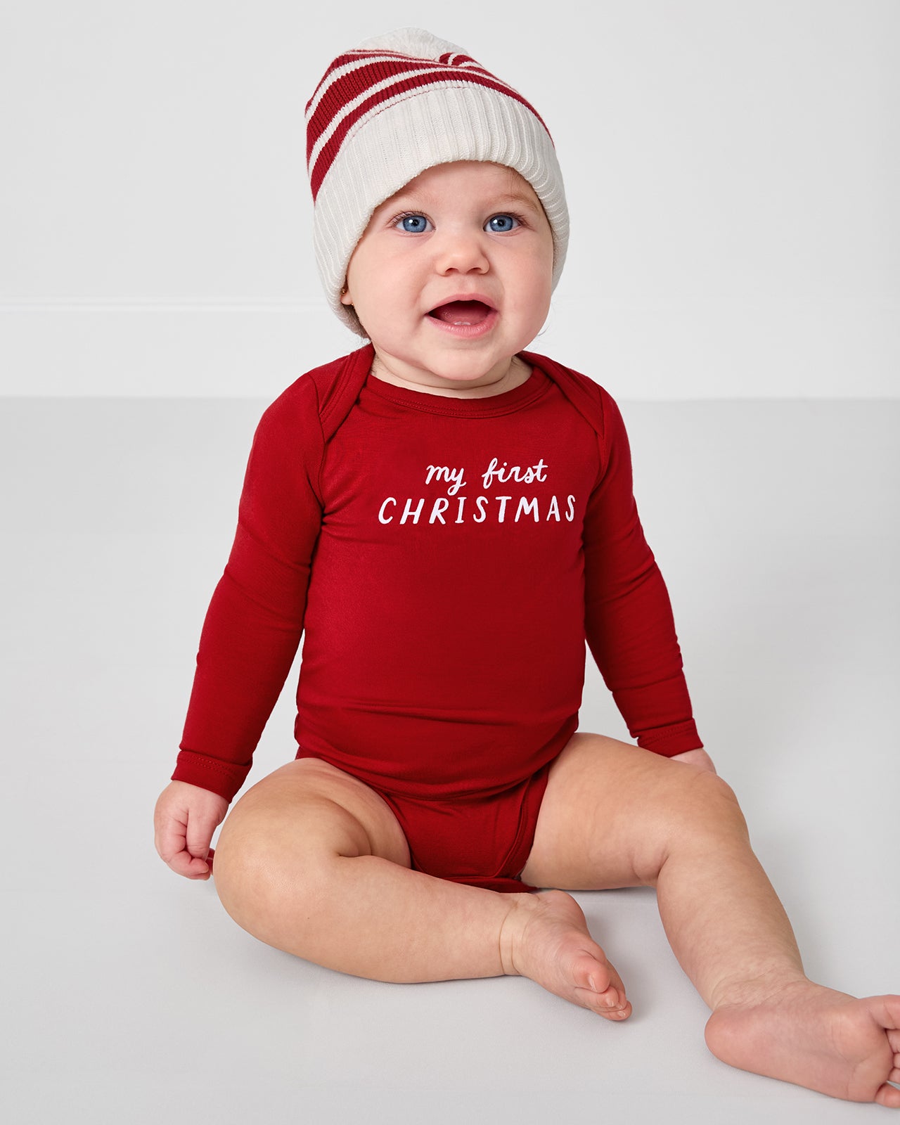 Baby wearing the My First Christmas Bodysuit with a red striped beanie
