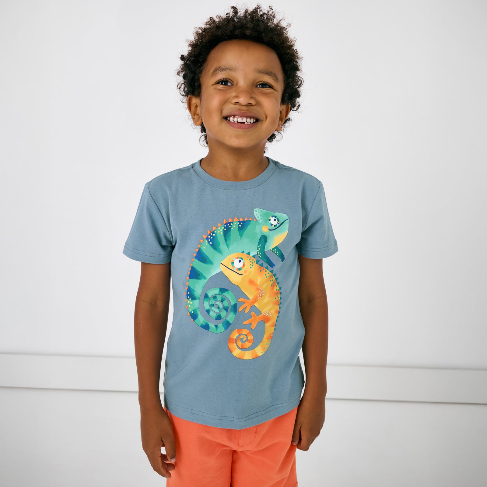 Standing child wearing the Chameleon Relaxed Tee with orange drawstring shorts