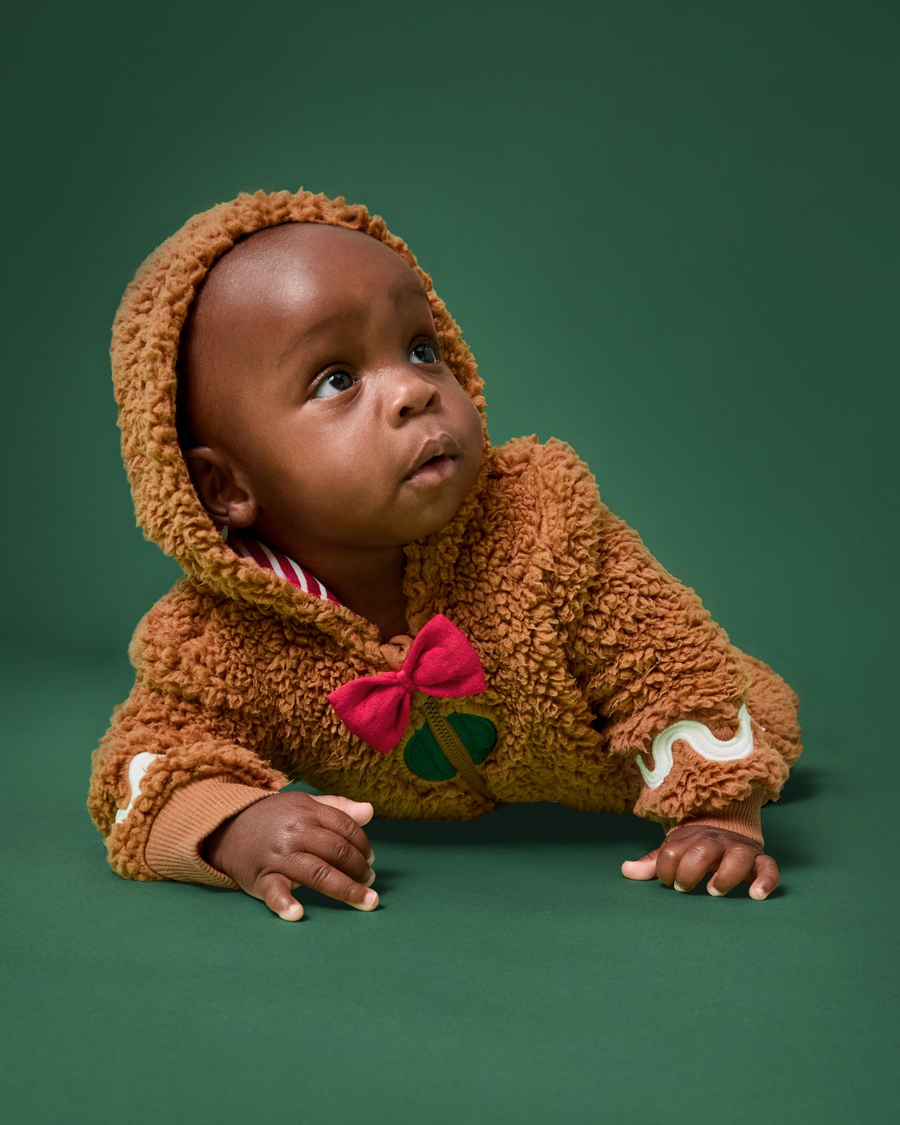 Crawling baby wearing the Gingerbread Sherpa Romper on a green background