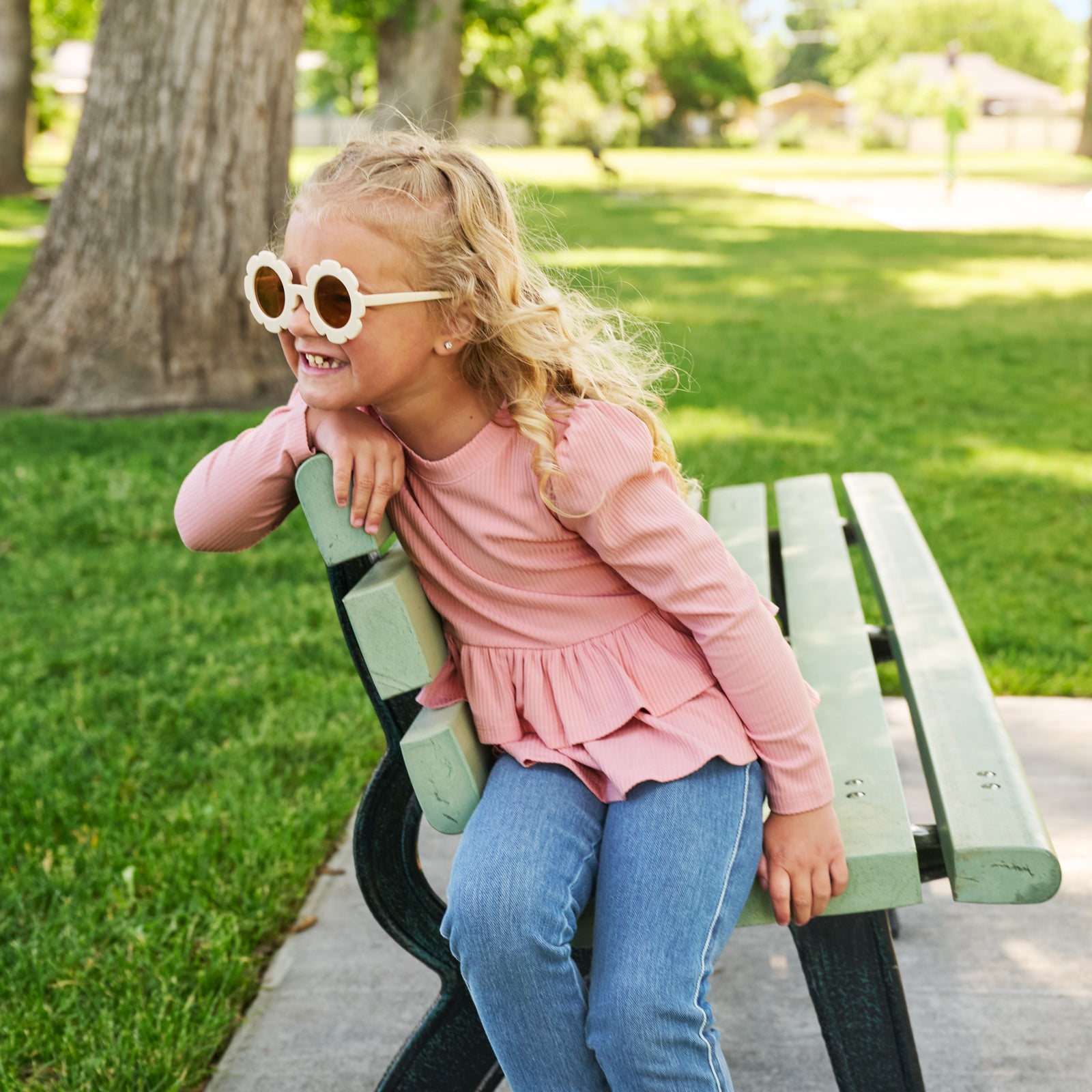 girl wearing midwash denim and mauve peplum top sitting on a park bench