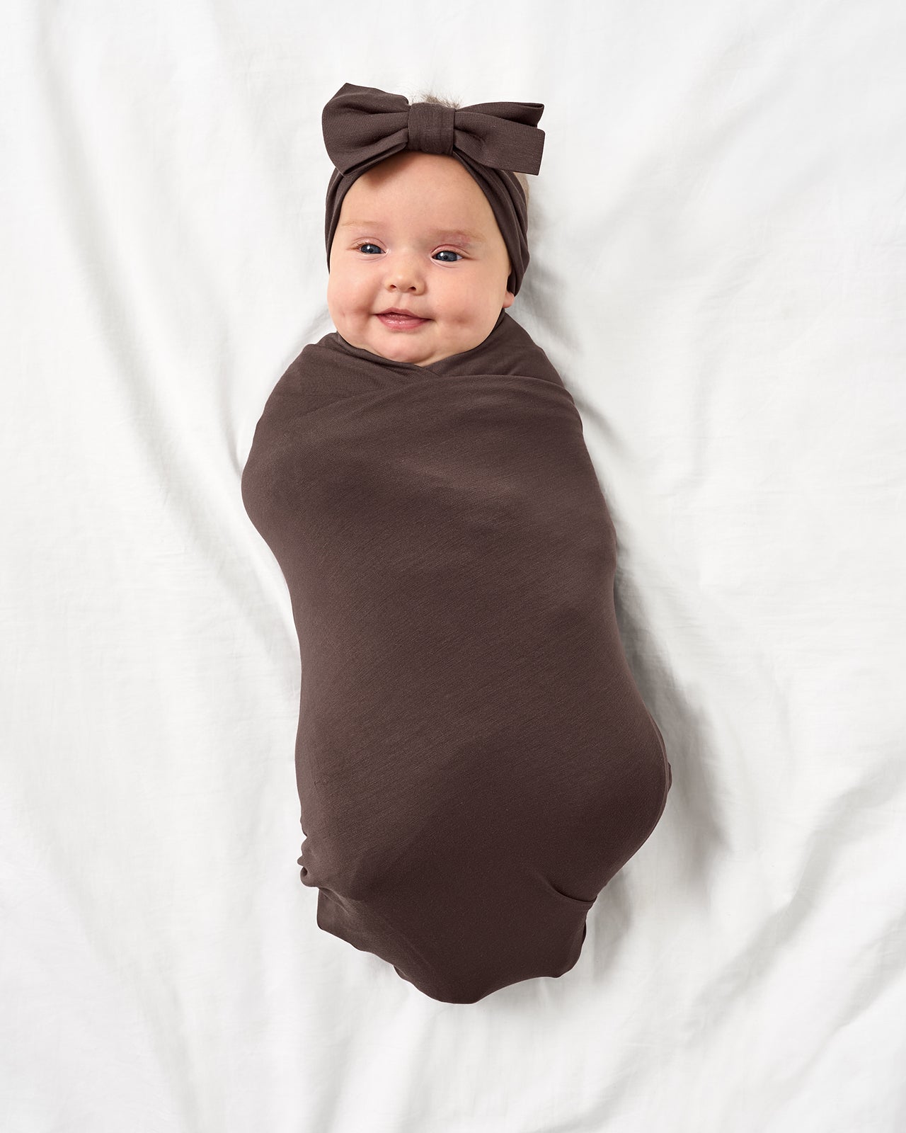 Baby wearing the Dark Chocolate Swaddle & Luxe Bow Headband Set