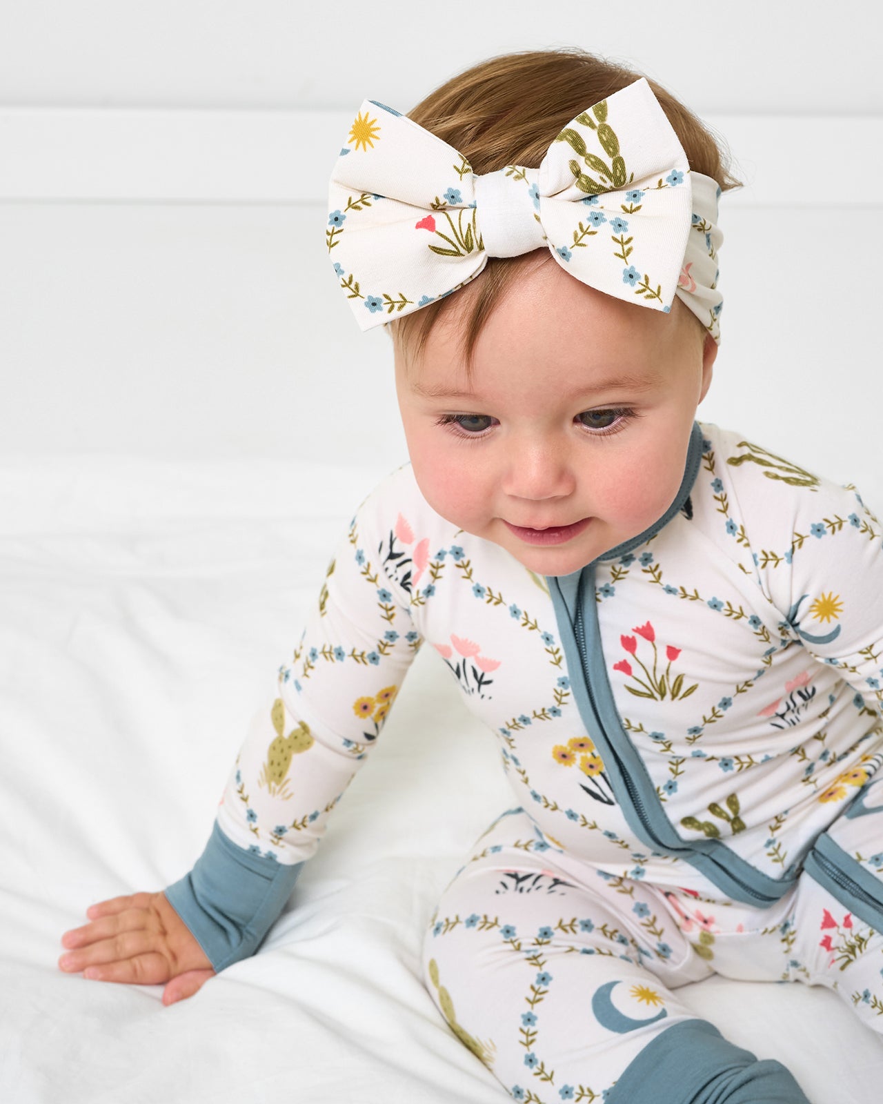 Baby sitting on a white bed wearing the Desert Meadow Luxe Bow Headband