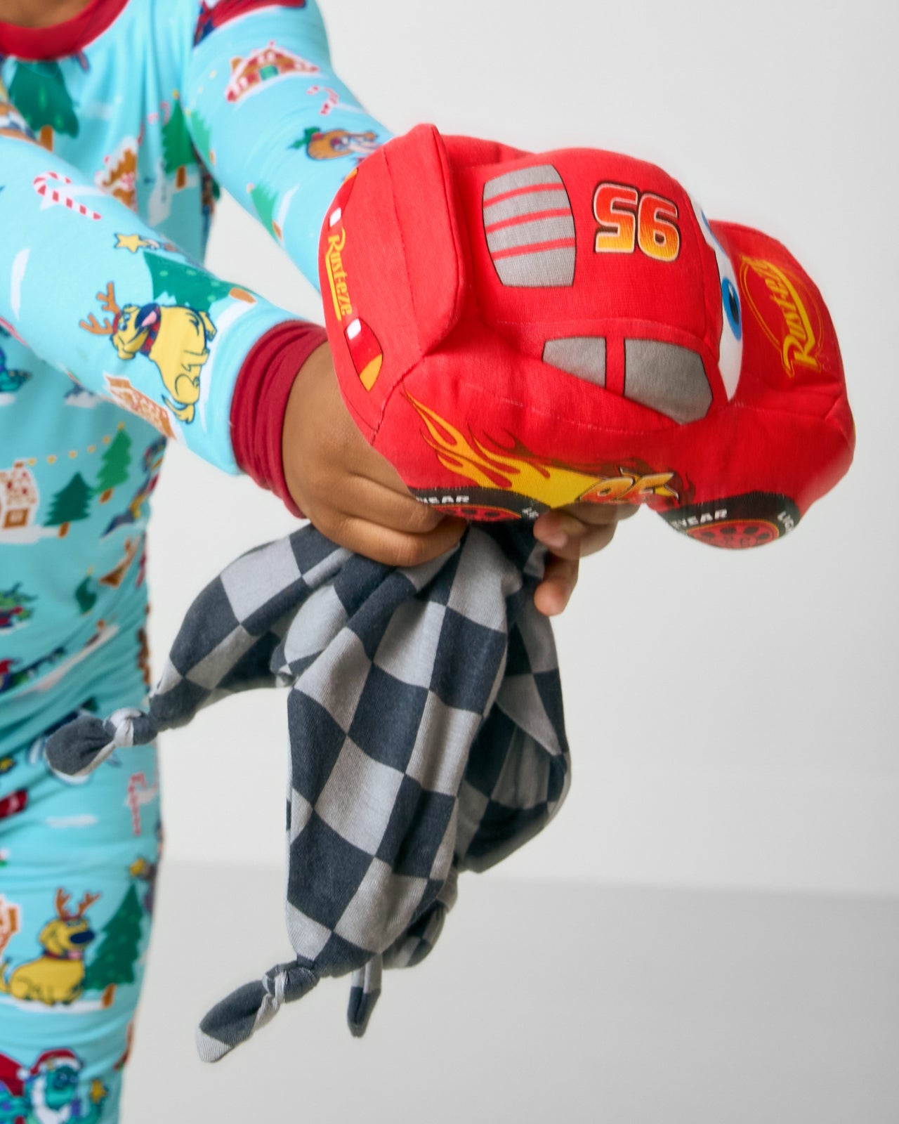 Child holding the Disney & Pixar Lightning McQueen Lovey wearing Christmas Village Pajamas