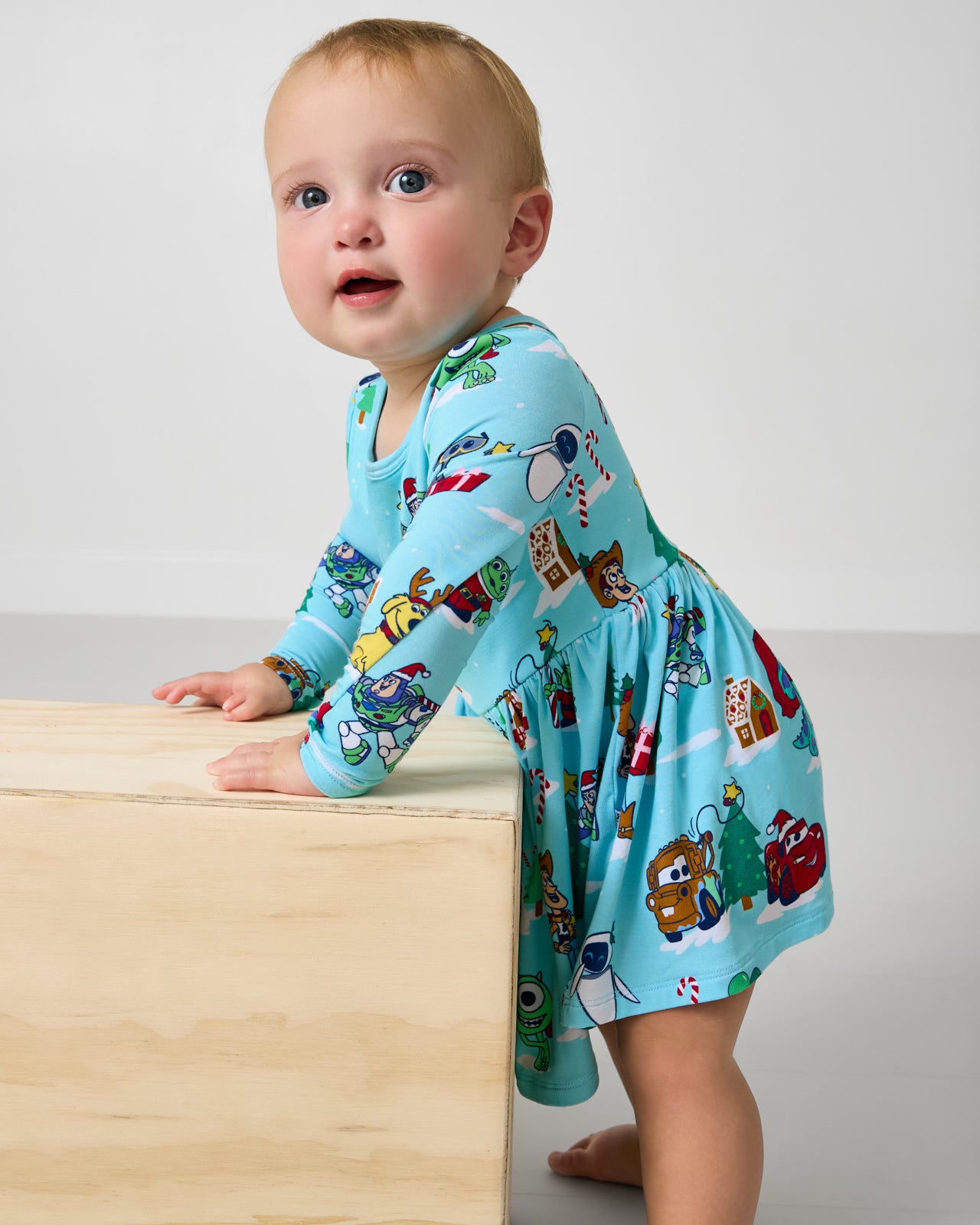 Standing baby wearing the Disney & Pixar Christmas Village Skater Dress with Bodysuit