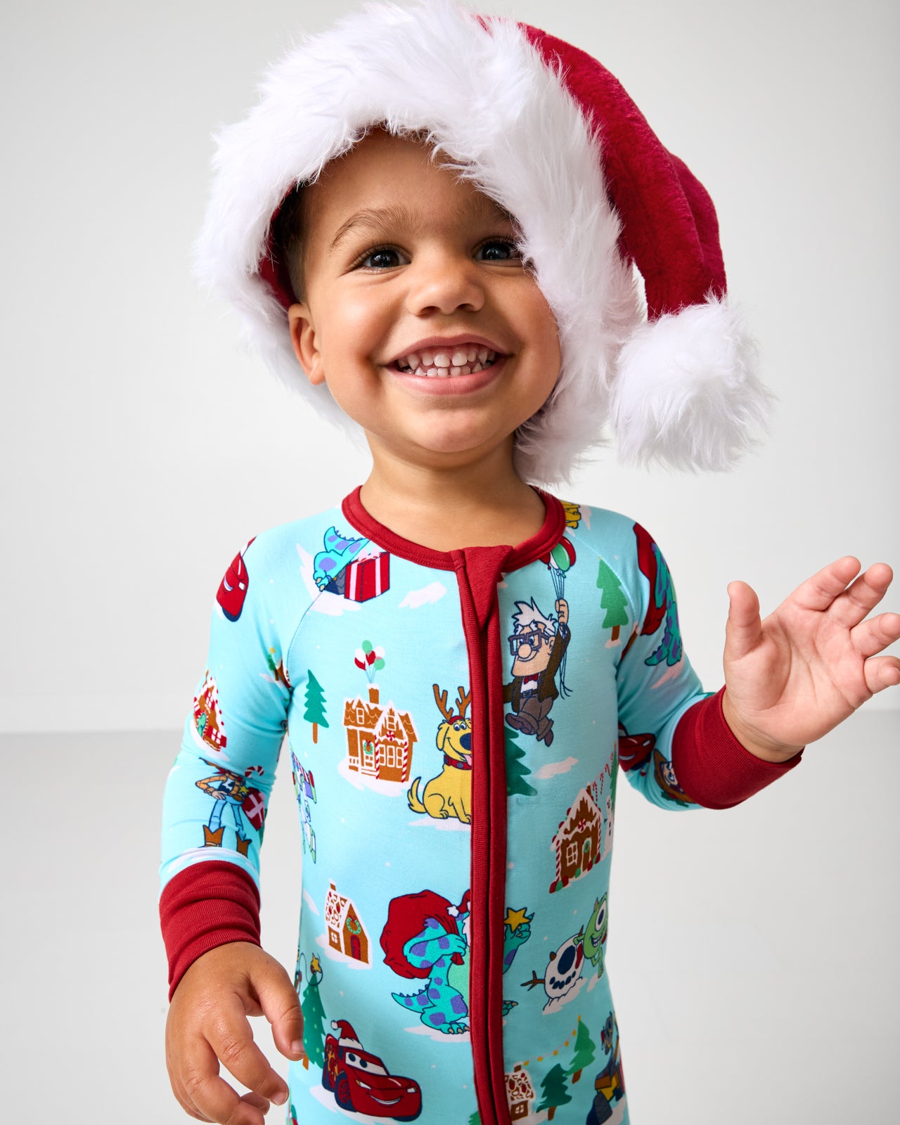 Child wearing a Santa hat and Christmas-themed onesie on a plain background