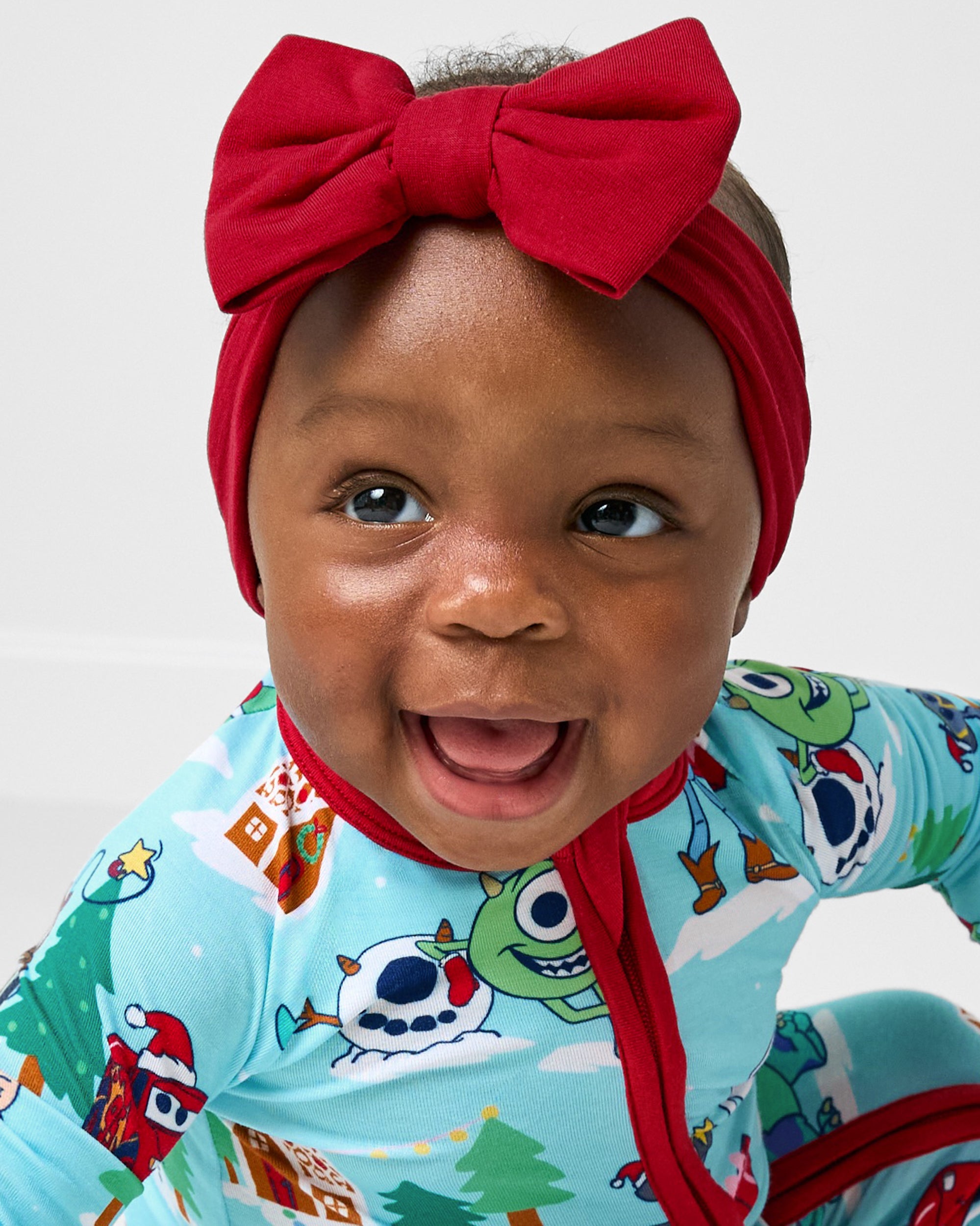 Baby wearing the Holiday Red Luxe Bow Headband with the Christmas Village zippy