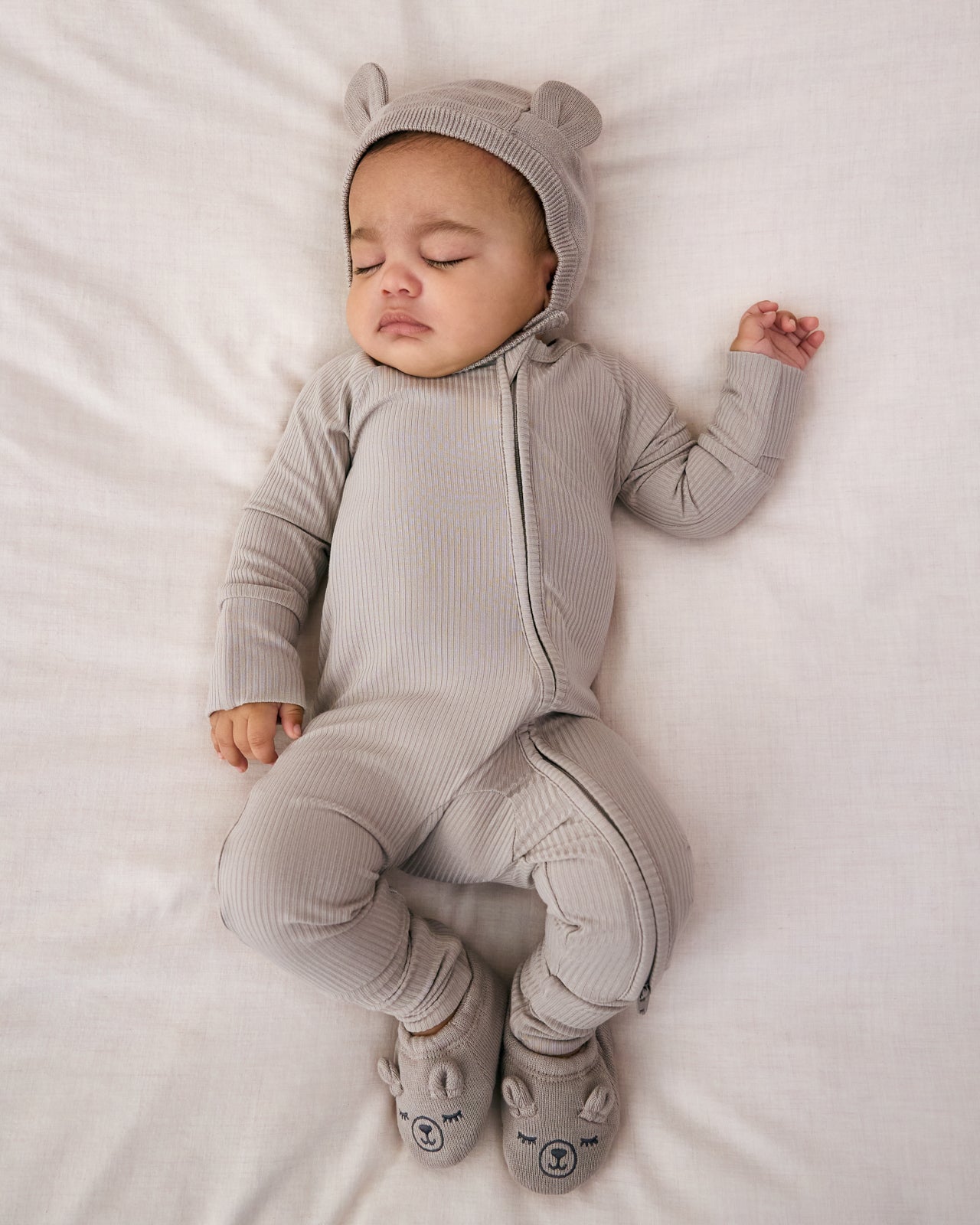 Sleeping newborn wearing the Dove Gray Bear Booties with a gray ribbed zippy