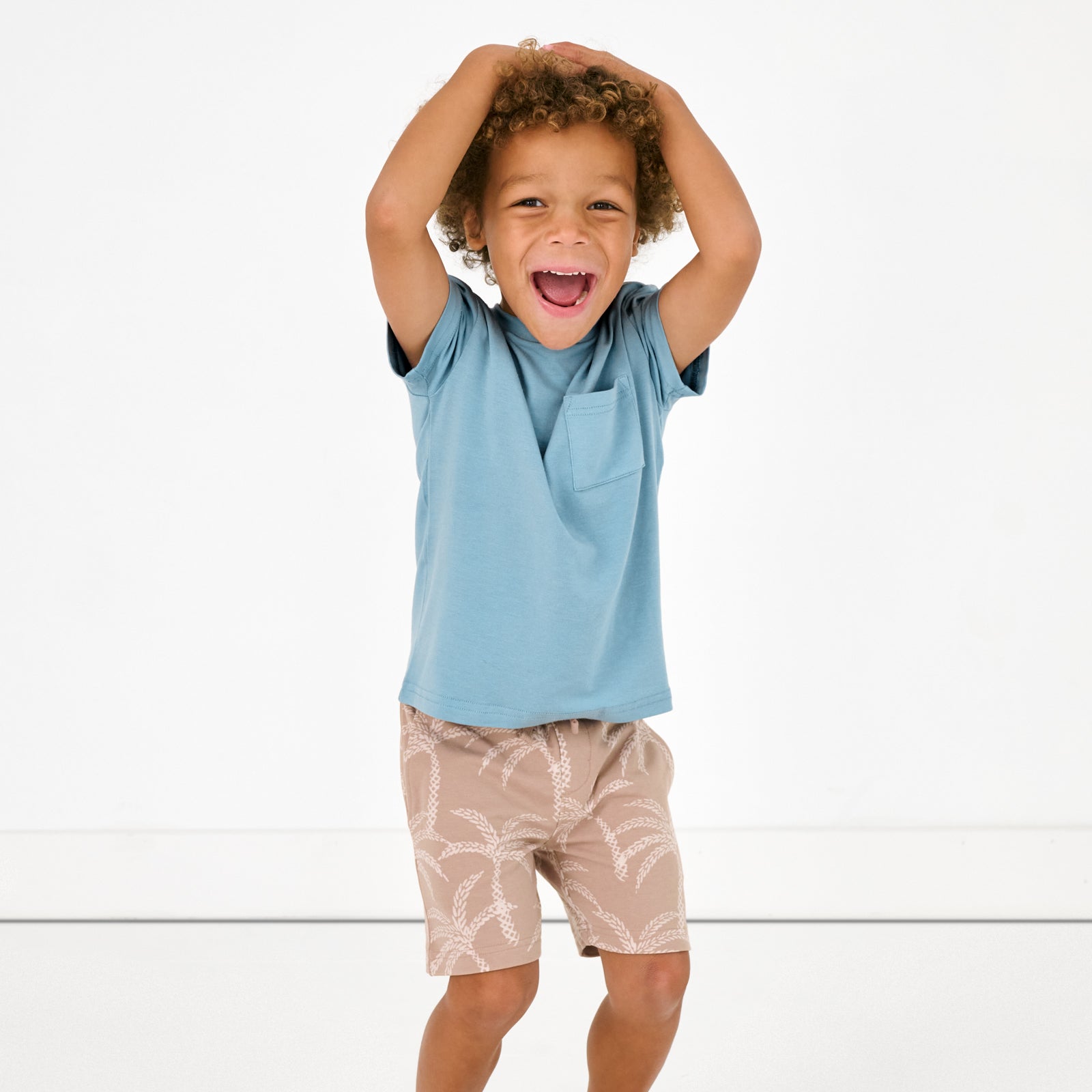 Standing child wearing the Dusk Blue Relaxed Pocket Tee with Sandy Palms shorts