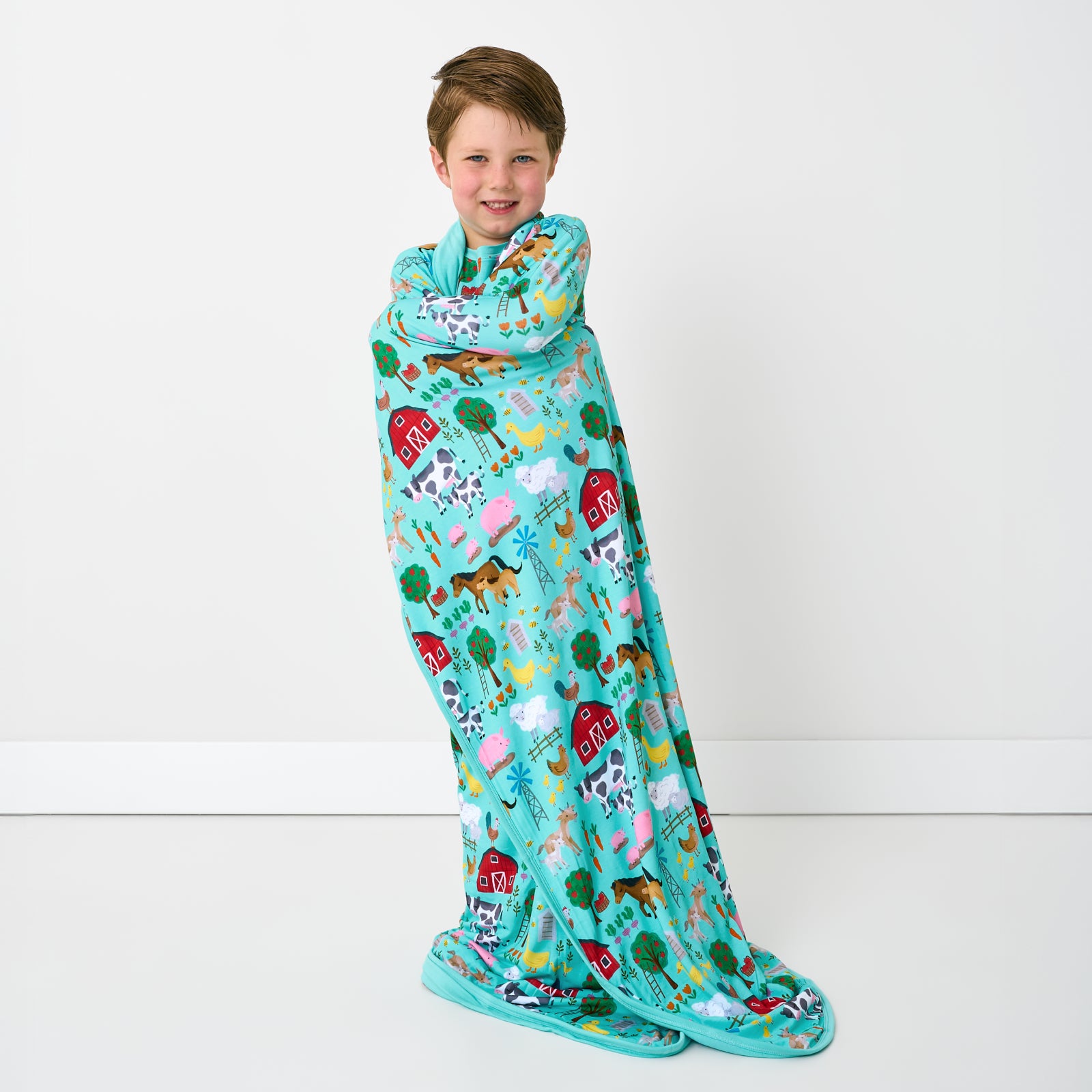 Standing child wrapped in the Turquoise Farm Fam Large Cloud Blanket®