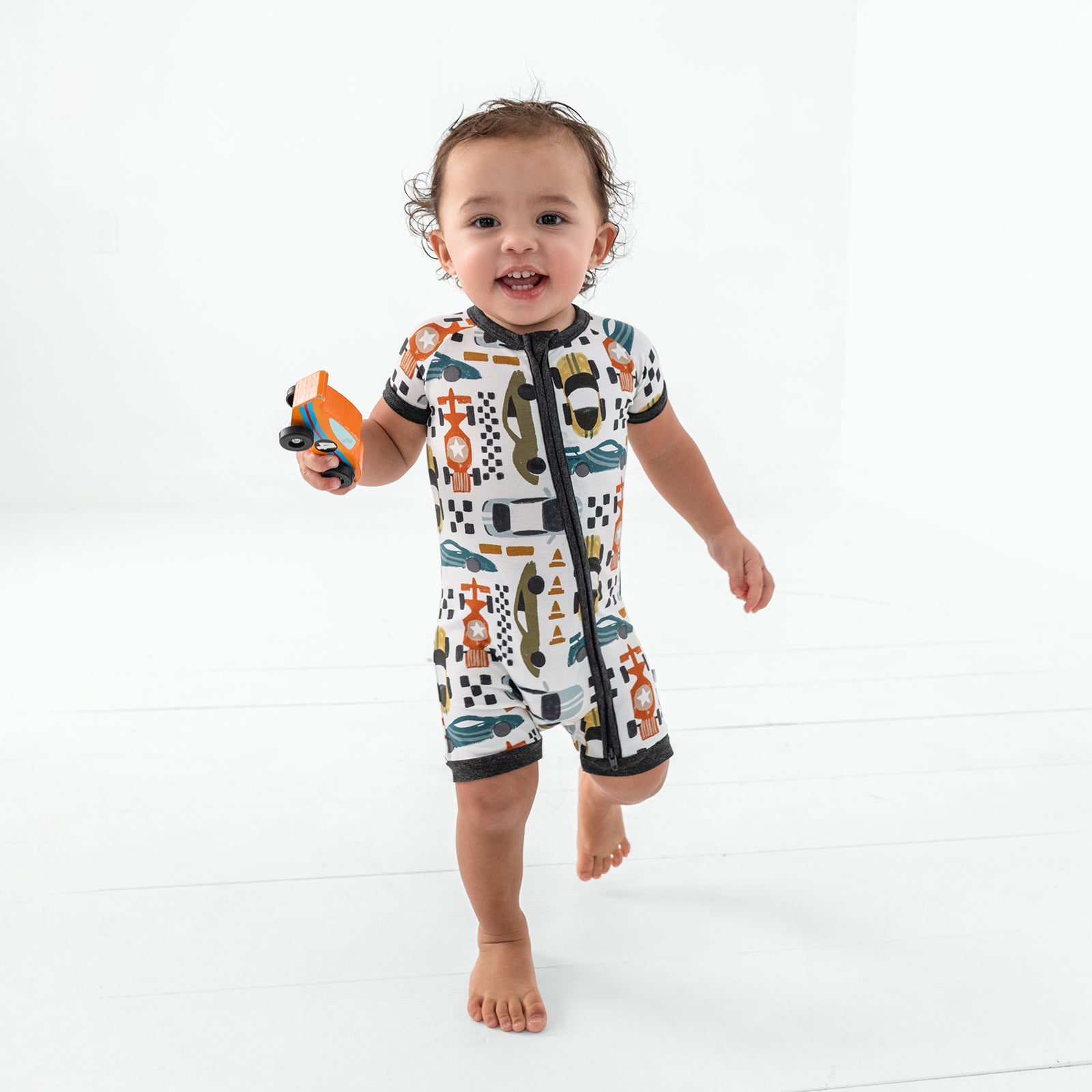 Walking toddler wearing the Fast Lane Shorty Zippy holding a race car toy