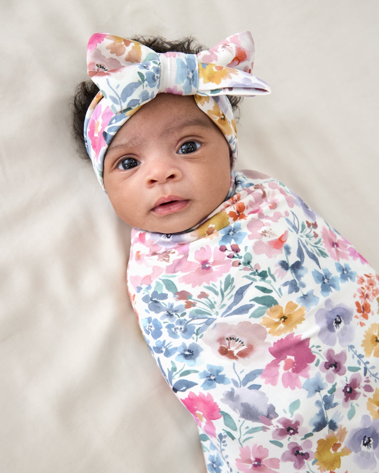 Close up of baby wrapped in the Tiny Blooms Swaddle & Luxe Bow Headband Set