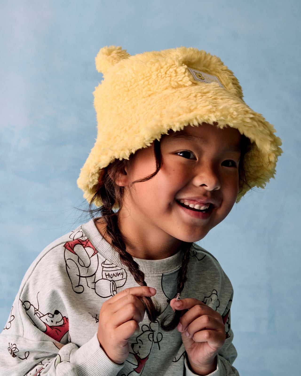 Alternate of girl wearing the Disney Winnie the Pooh Sherpa Bucket Hat on a blue background
