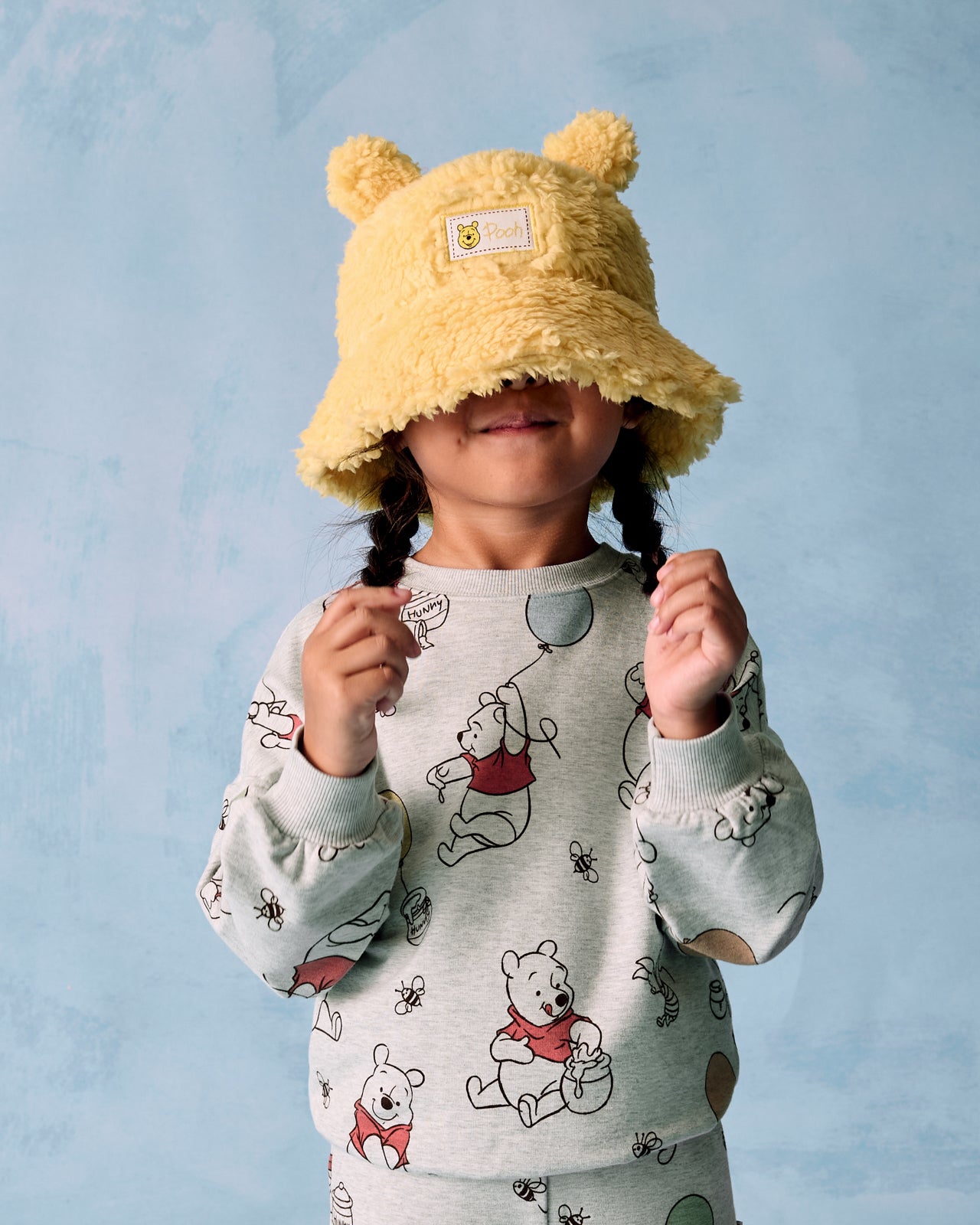 Girl wearing the Disney Winnie the Pooh Sherpa Bucket Hat on a blue background