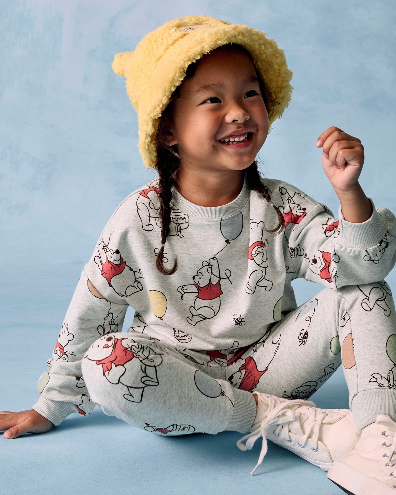 Sitting girl wearing the Disney Up, Up and Away Jogger and Crewneck on the blue background