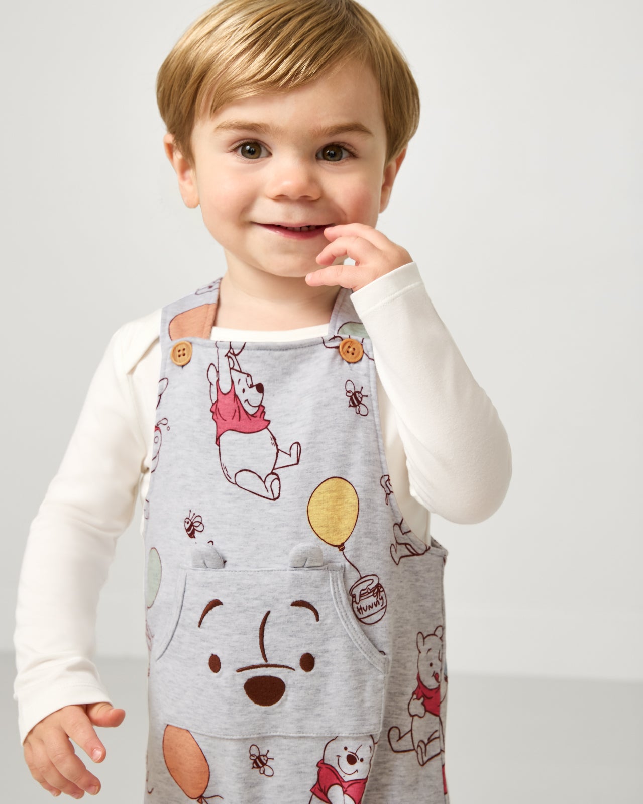 Close up of boy wearing the Disney Up, Up and Away Overall layered over a white bodysuit