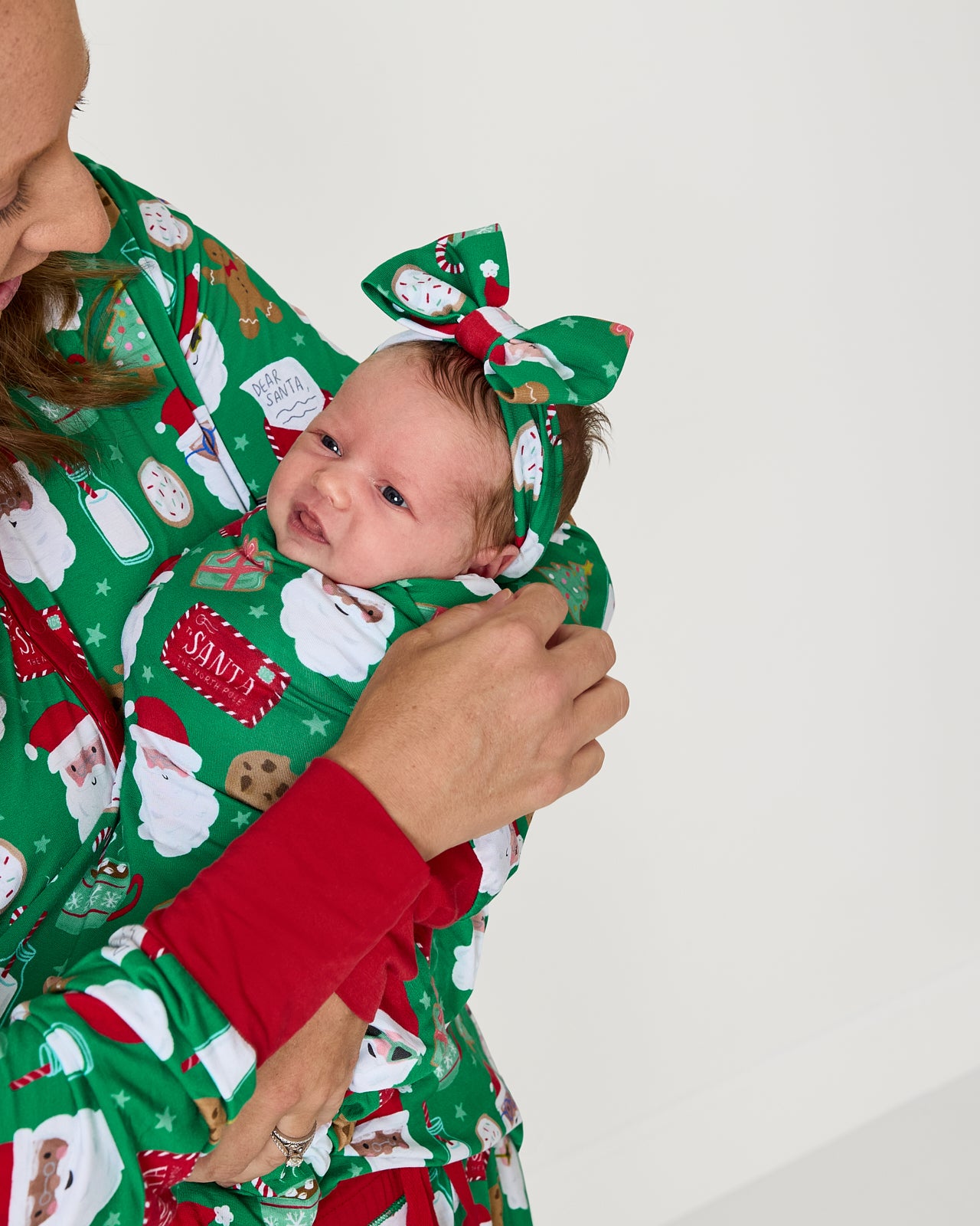 Mother holding baby wearing the Cookies for Santa Swaddle & Luxe Bow Headband Set