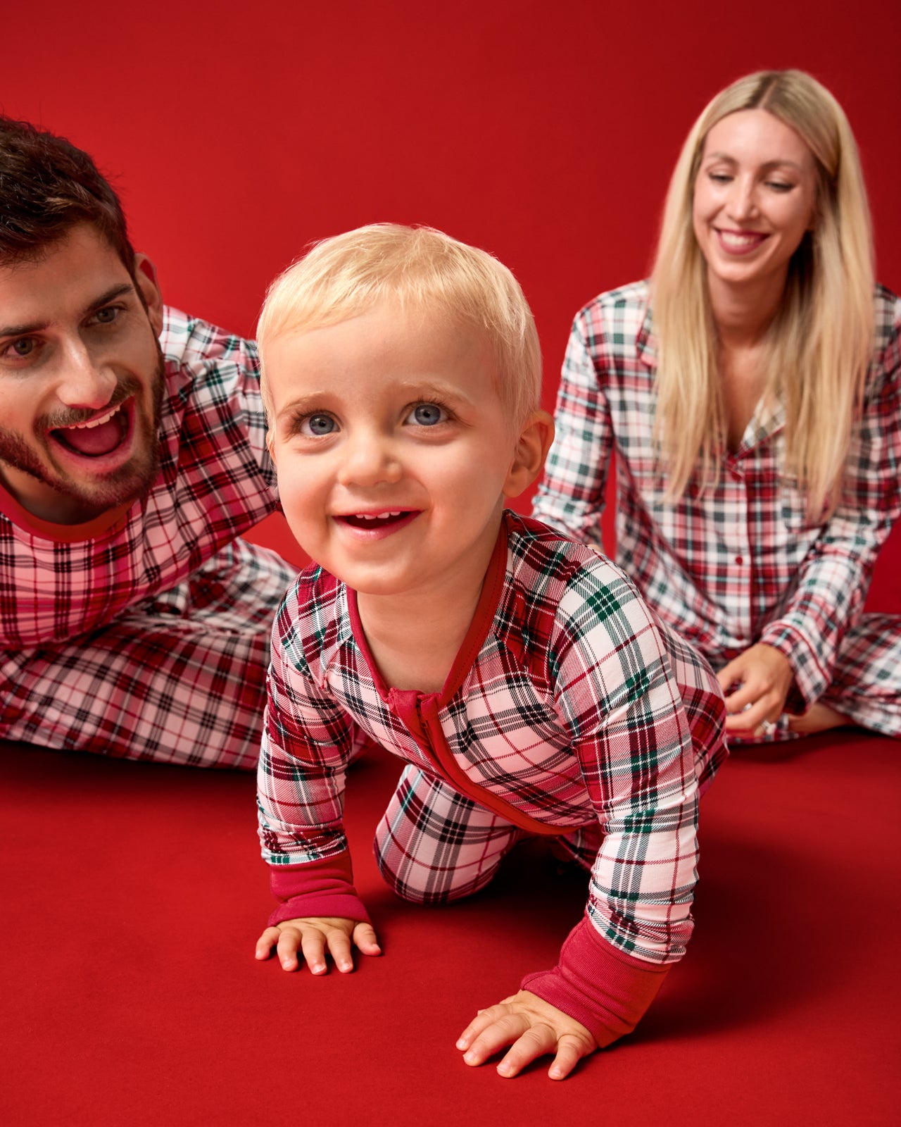 Family of three wearing Holly Plaid pajamas on a red background