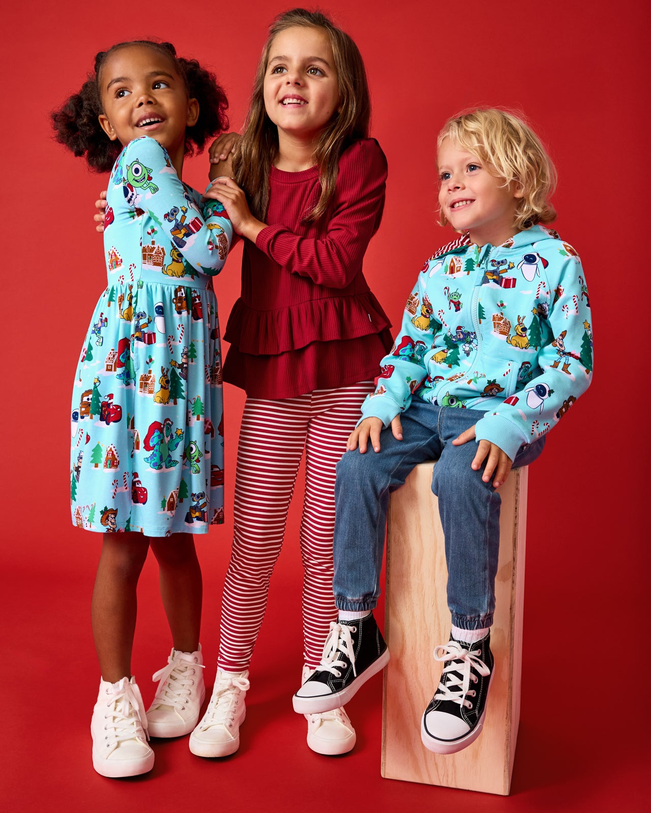 Three kids wearing styles from the Holiday Collection on a red background