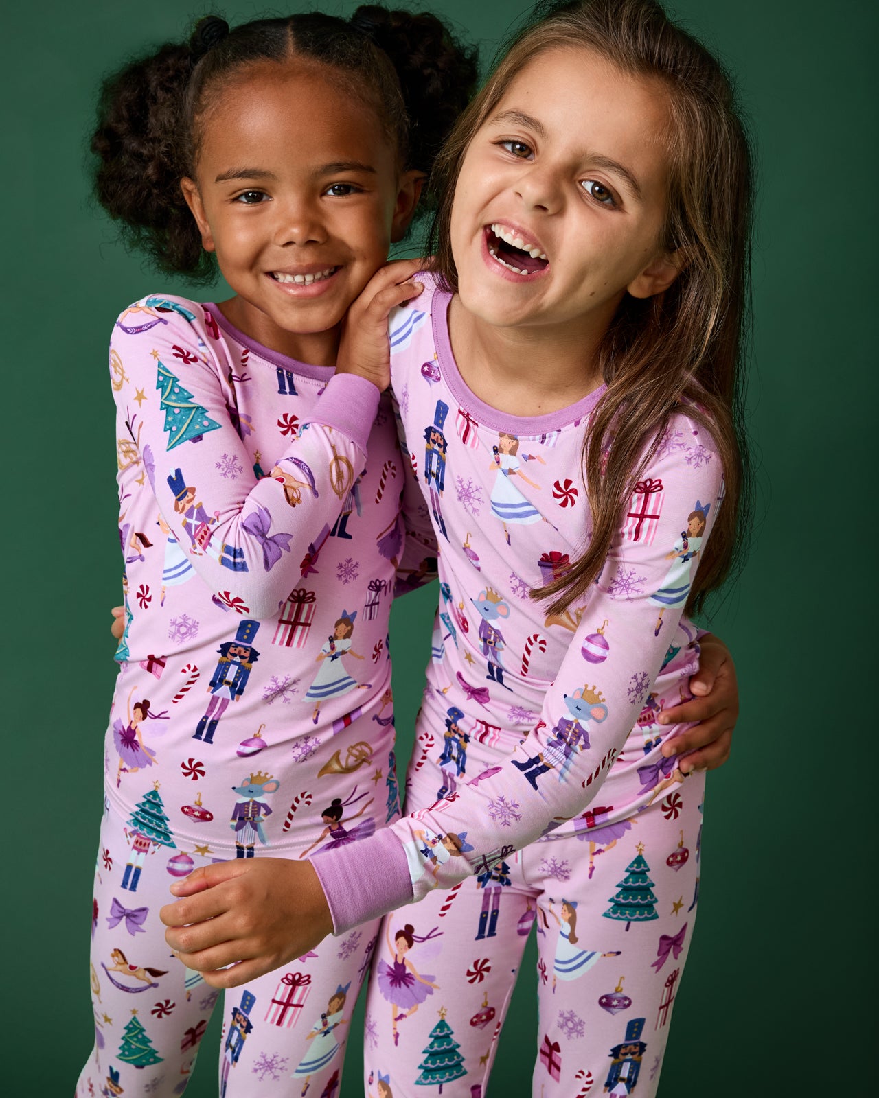 Two girls wearing Nutcracker themed PJs on a green background