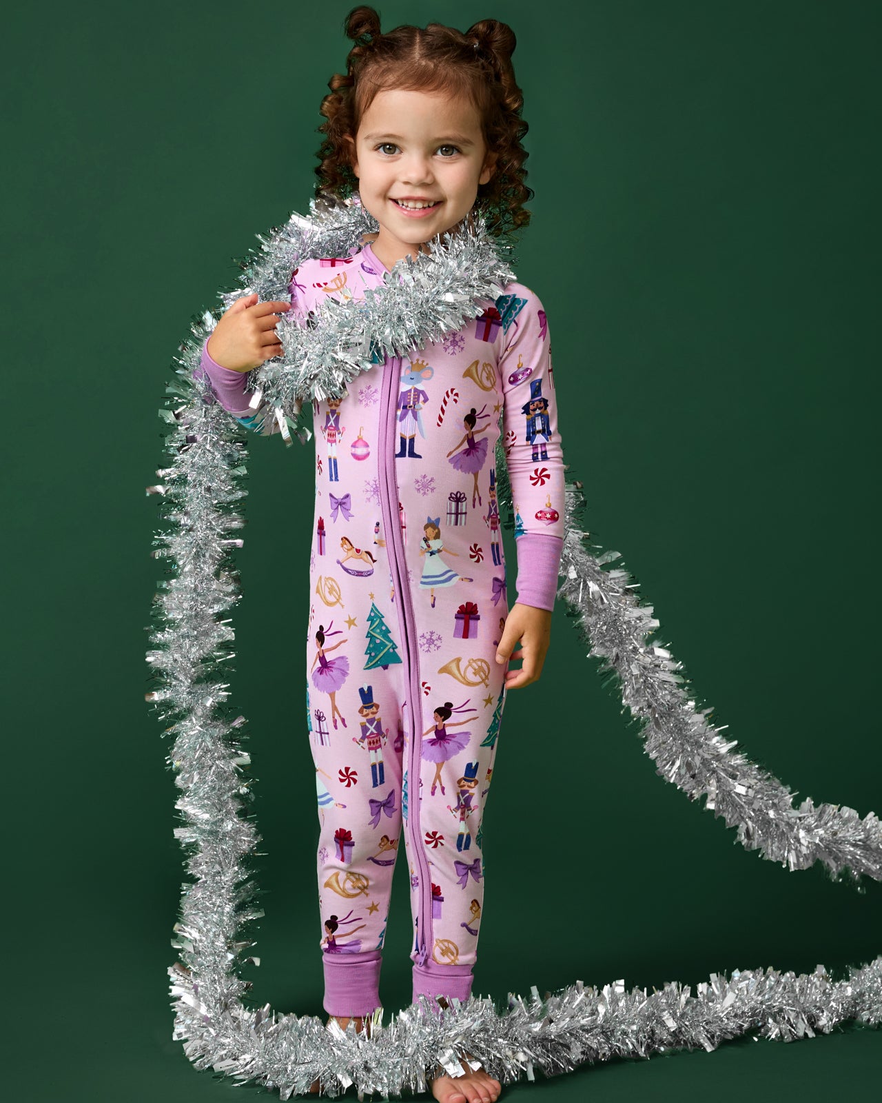 Child wearing a pink Nutcracker zippy wrapped in tinsel on a green background