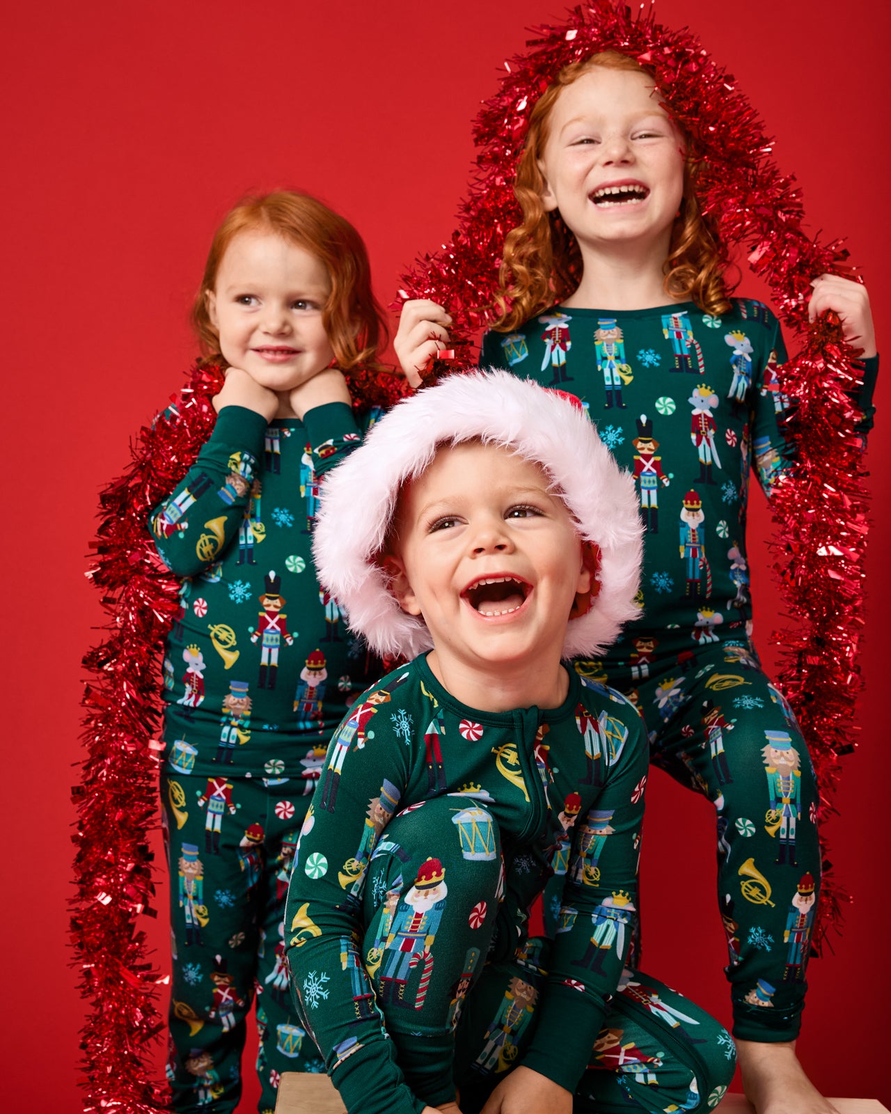 Three children wearing matching Nutcracker March PJs on a red background