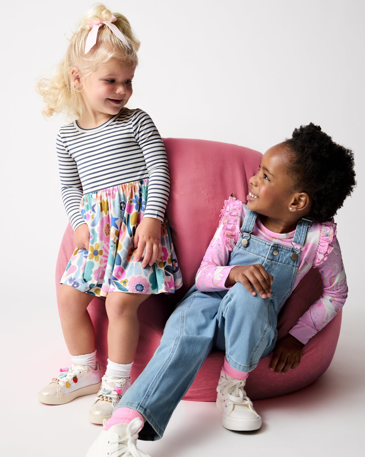 Two girls on a pink ottoman wearing styles from the Winter Play drop