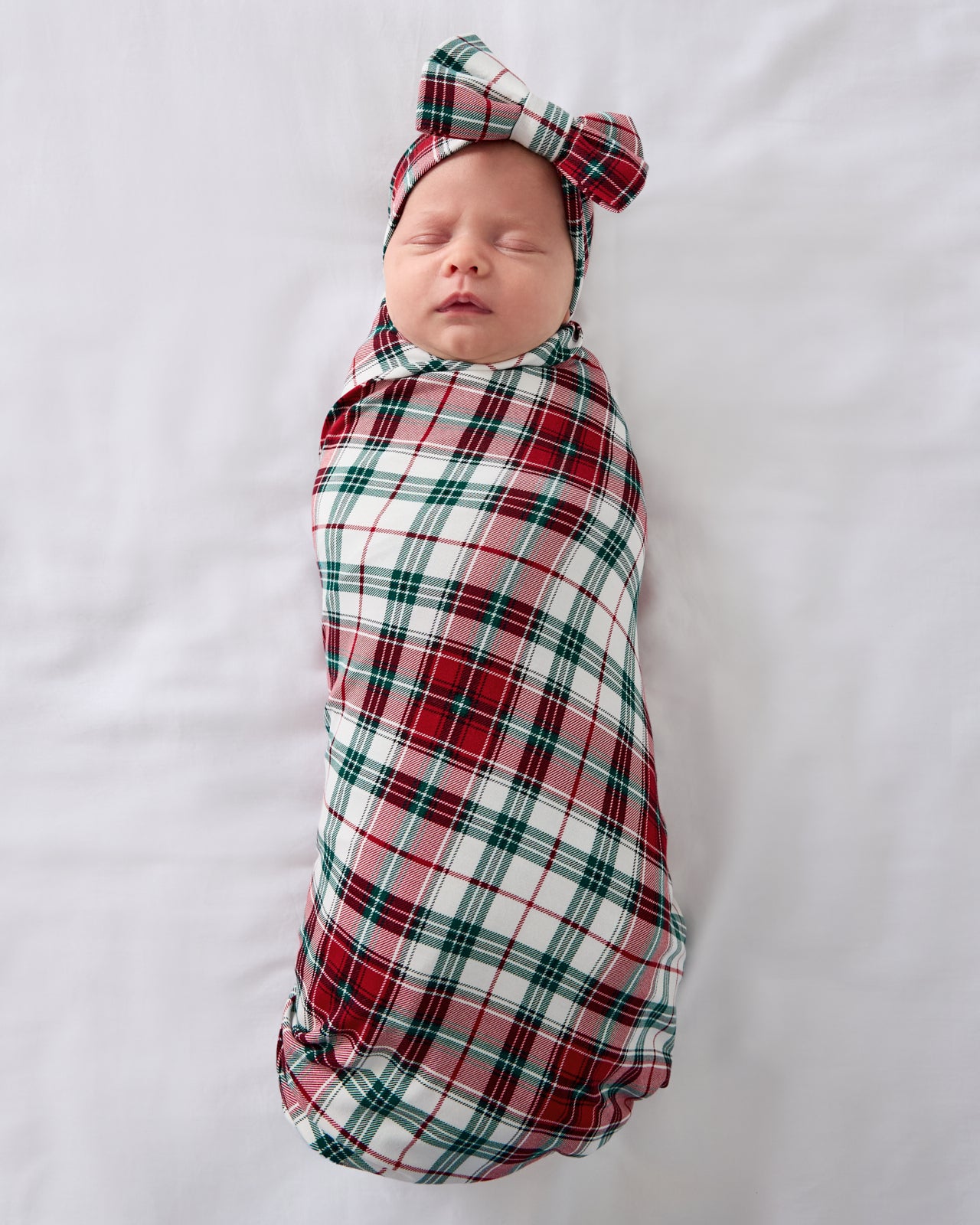 Aerial view of baby wearing the Holly Plaid Swaddle & Luxe Bow Headband Set
