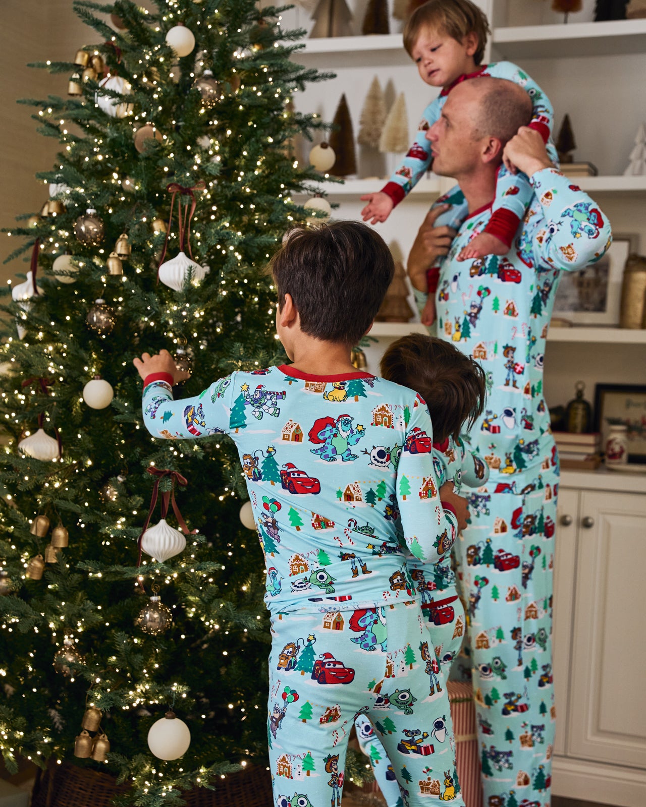 Family wearing matching Disney & Pixar Christmas Village pajamas decorating a tree