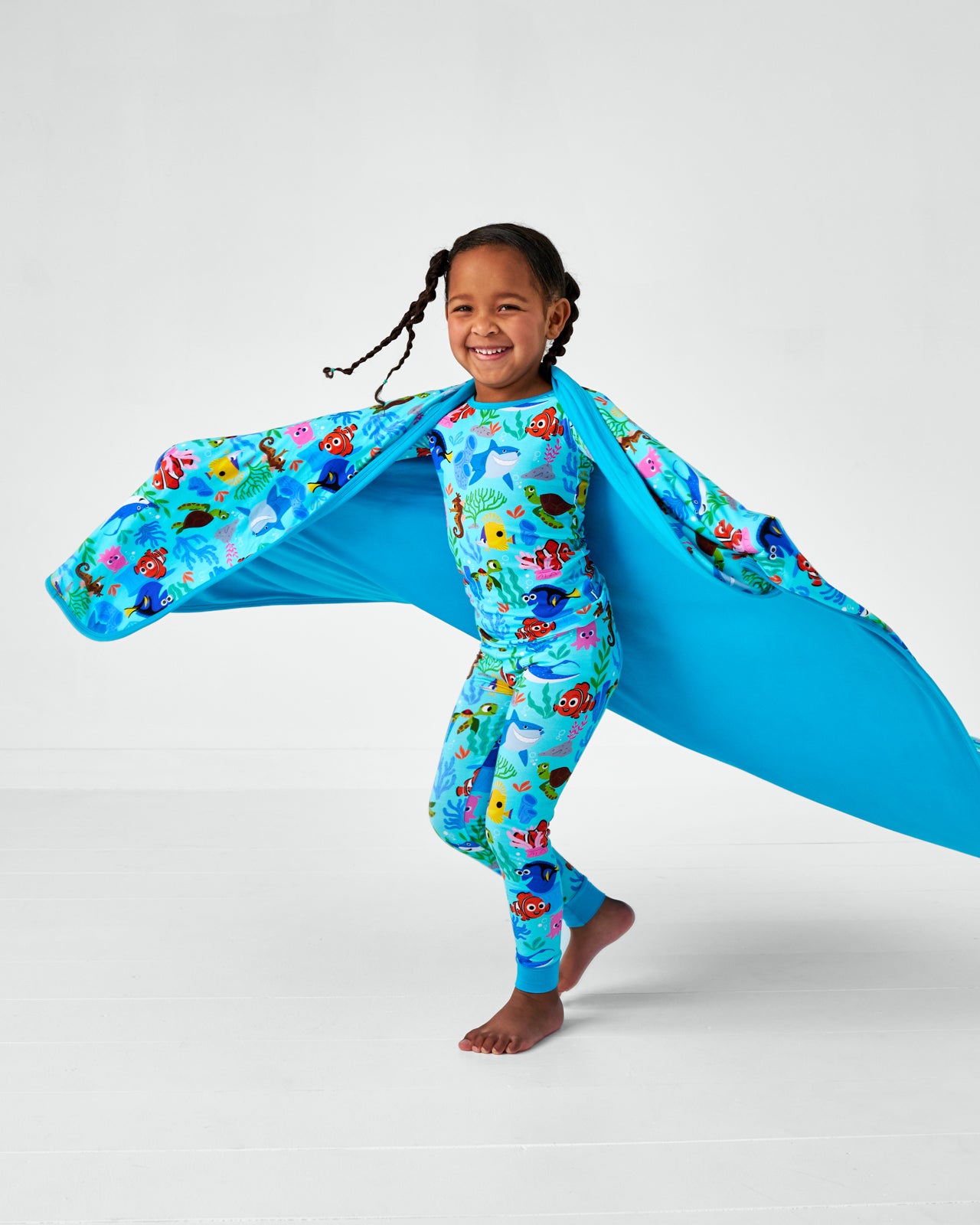Child wearing the Nemo's Reef Two-Piece bamboo pjs with the Disney Nemo's Reef Large Cloud Blanket® on her shoulders