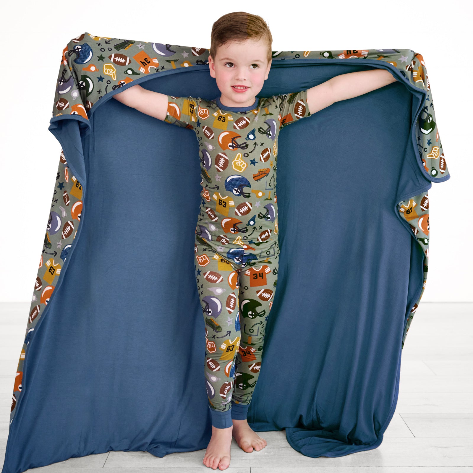 Boy posing with the Touchdown Time Large Cloud Blanket® while showing the inside blue color. He is wearing the touchdown-time-two-piece-short-sleeve-pajama-set