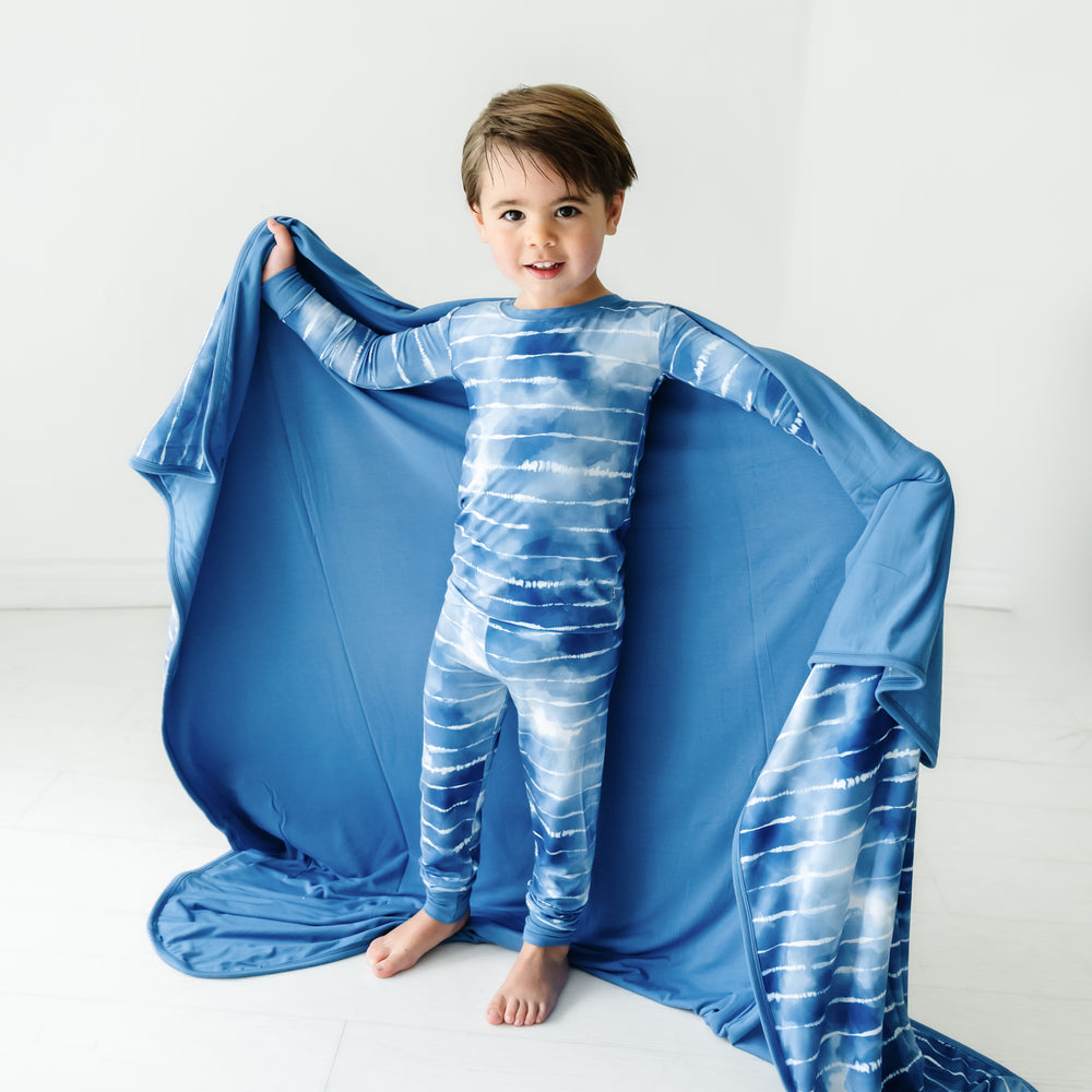 Child holding out a Blue Tie Dye Dreams large cloud blanket behind them, detailing the solid blue backing, and wearing matching pajamas