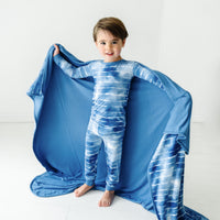 Child holding out a Blue Tie Dye Dreams large cloud blanket behind them, detailing the solid blue backing, and wearing matching pajamas