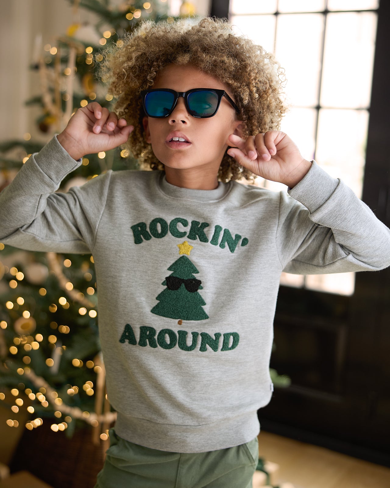 Boy wearing the Rockin' Around Crewneck Sweatshirt in front of a Christmas tree