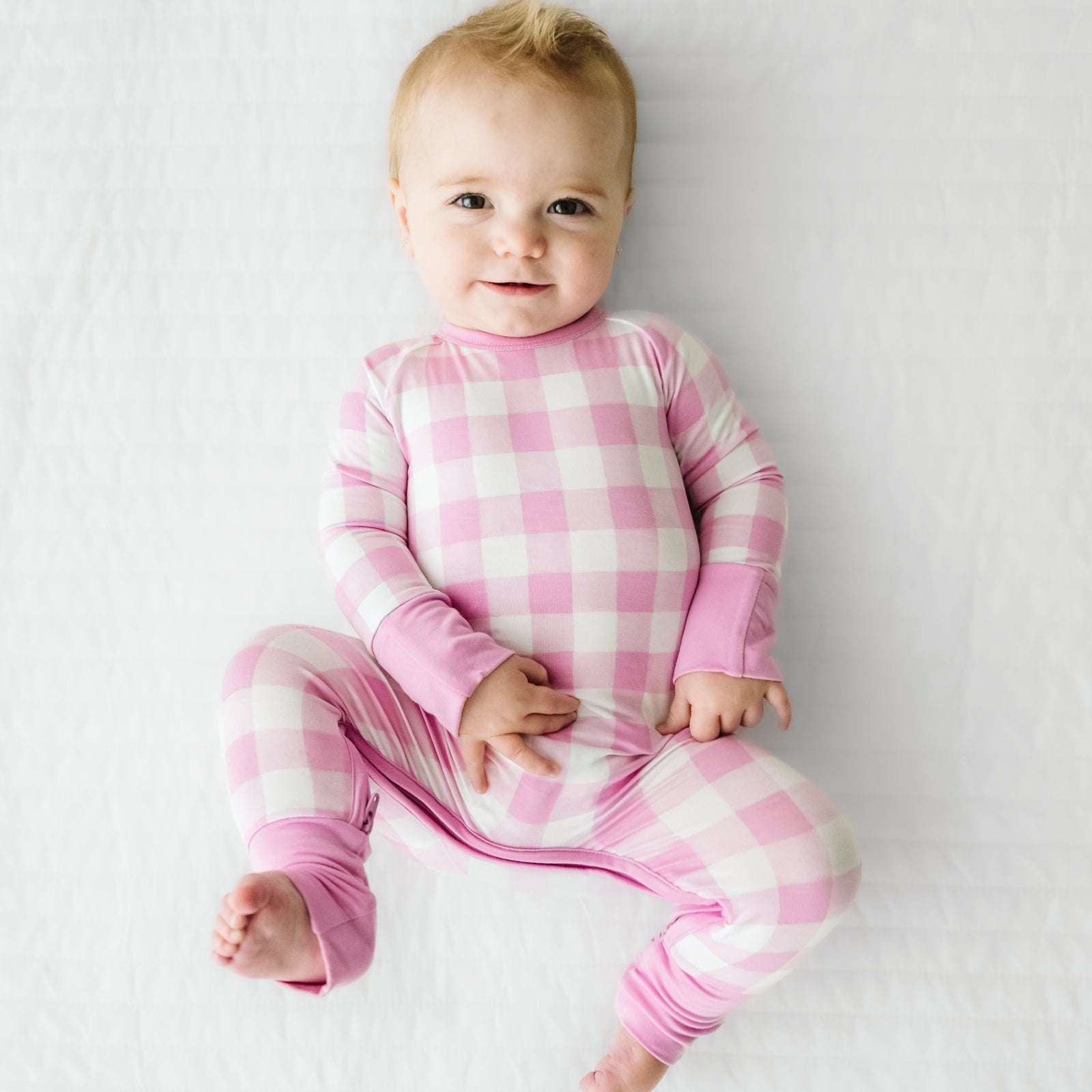 Child laying on a bed wearing a Pink Gingham crescent zippy